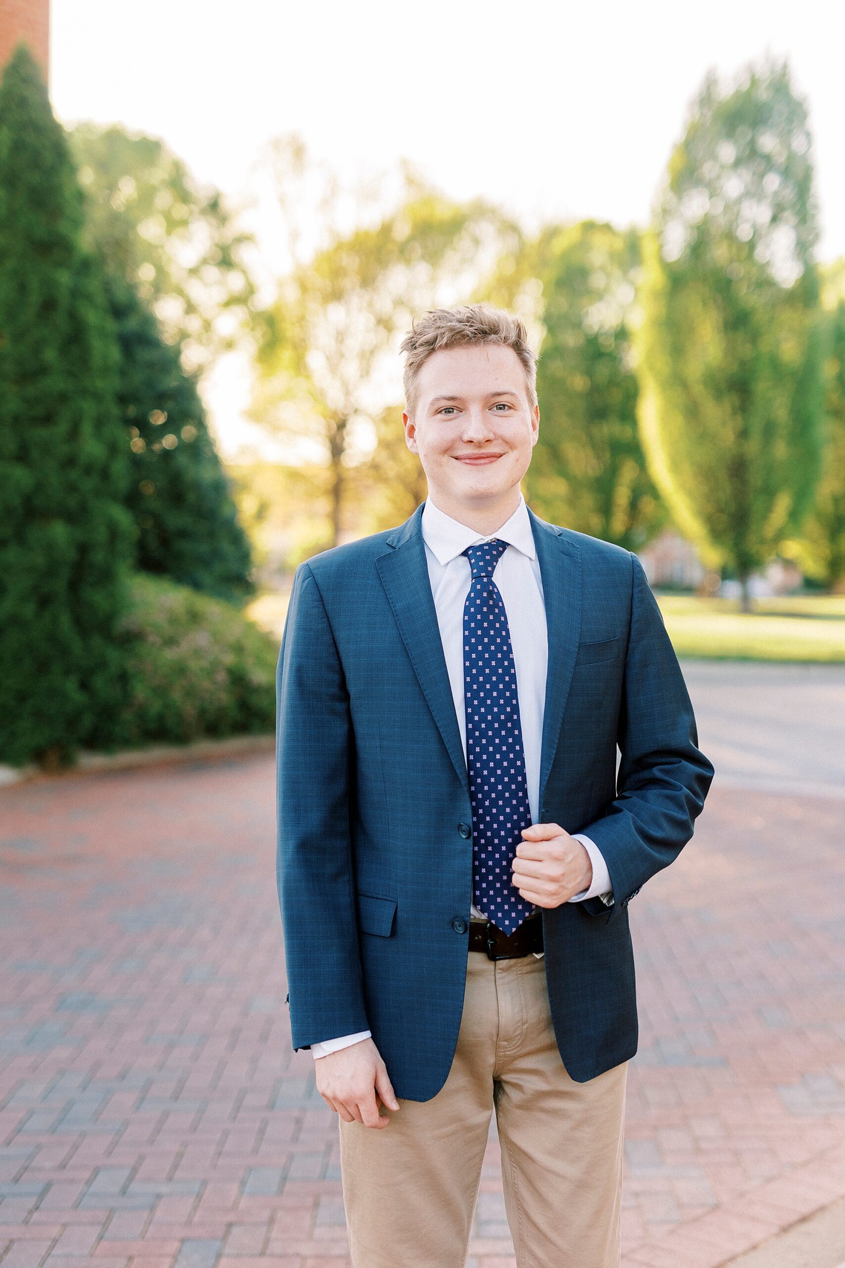 senior guy in navy blazer and tie holds lapel of jacket during UNC Charlotte senior portraits