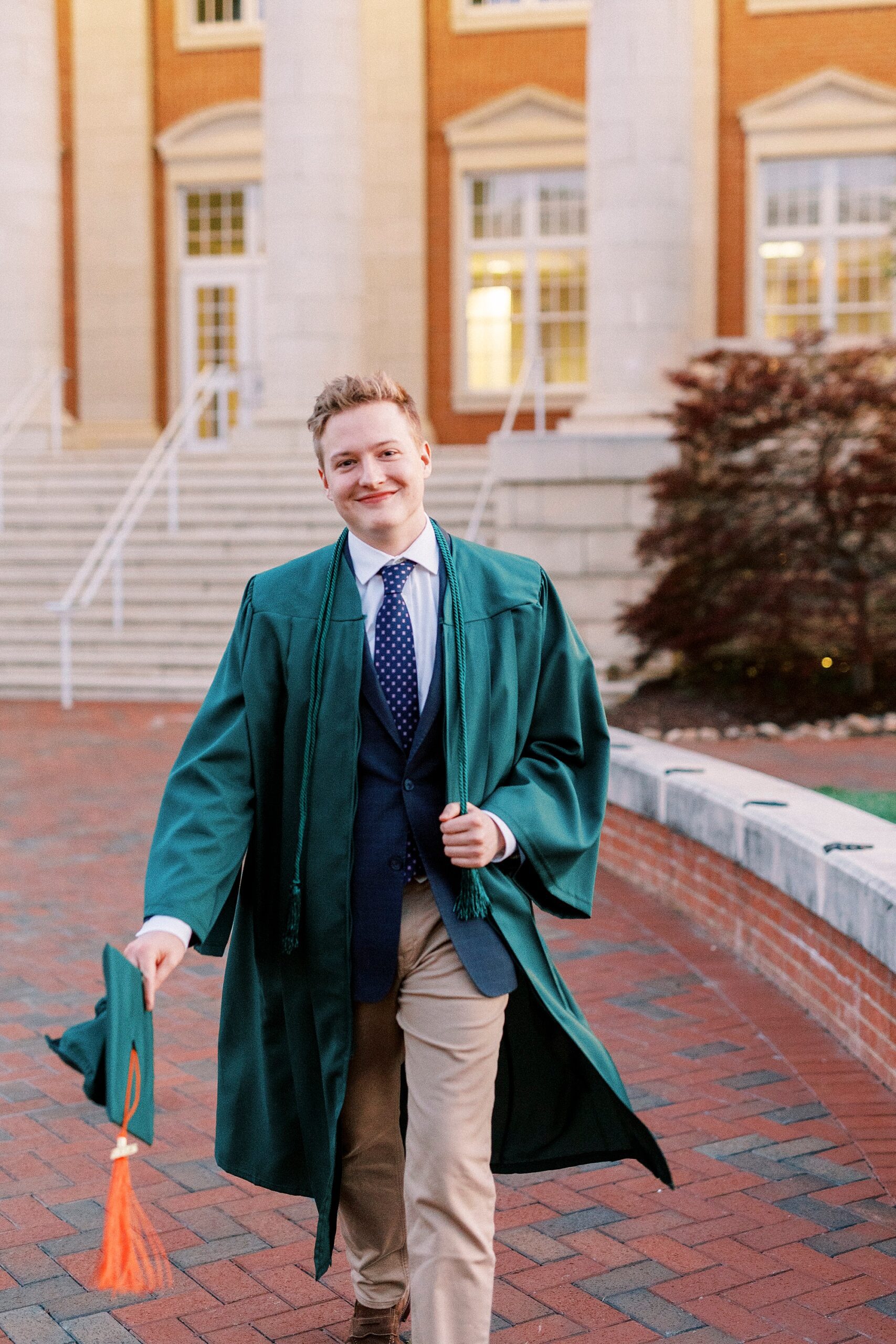 senior walks swinging green hat outside building during UNC Charlotte senior portraits