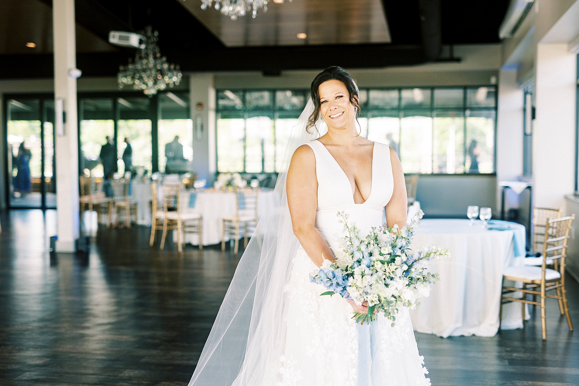 bride holds bouquet of white and blue flowers with veil behind her inside the Terrace at Cedar Hill