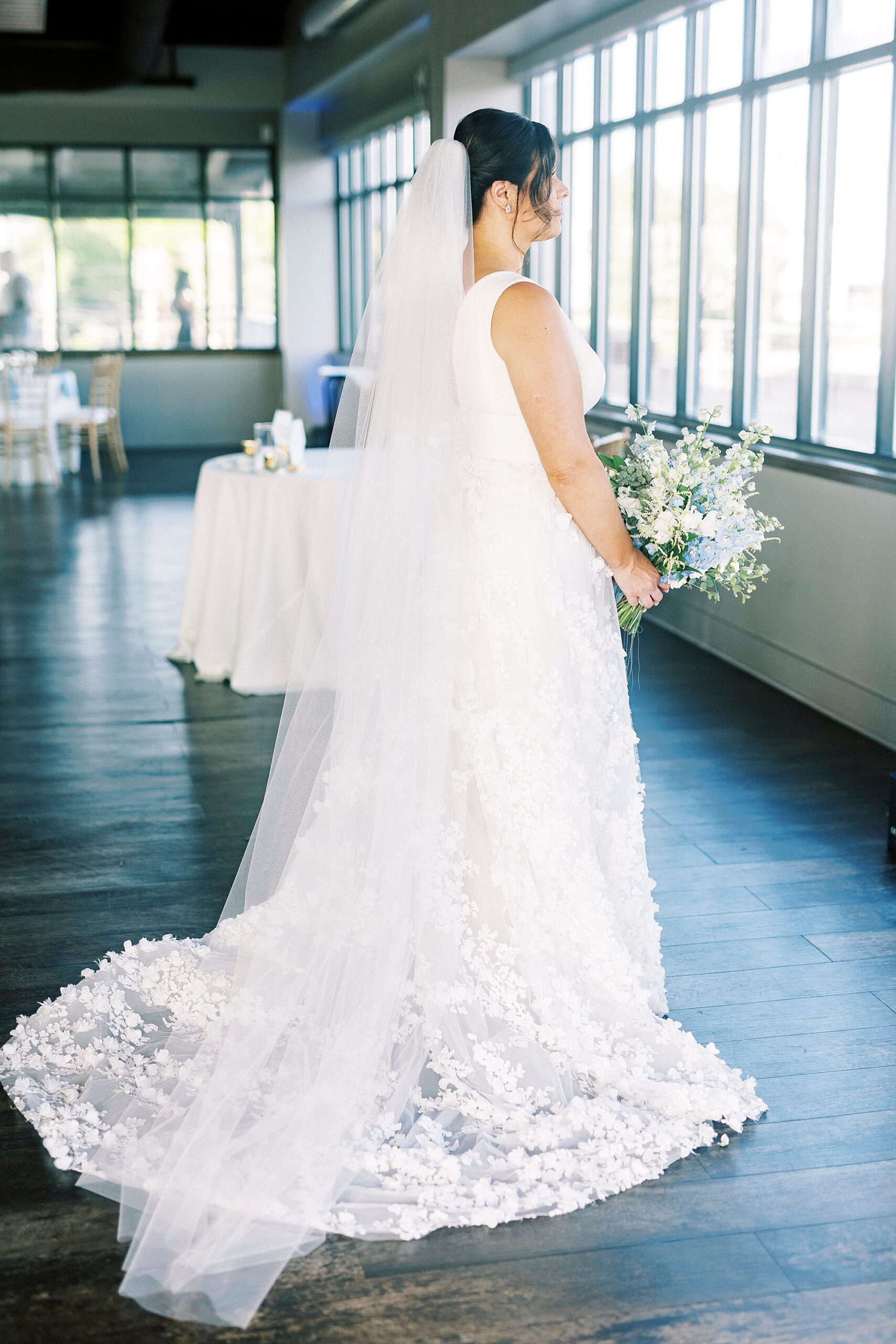 bride stands holding bouquet of white and blue flowers inside the Terrace at Cedar Hill