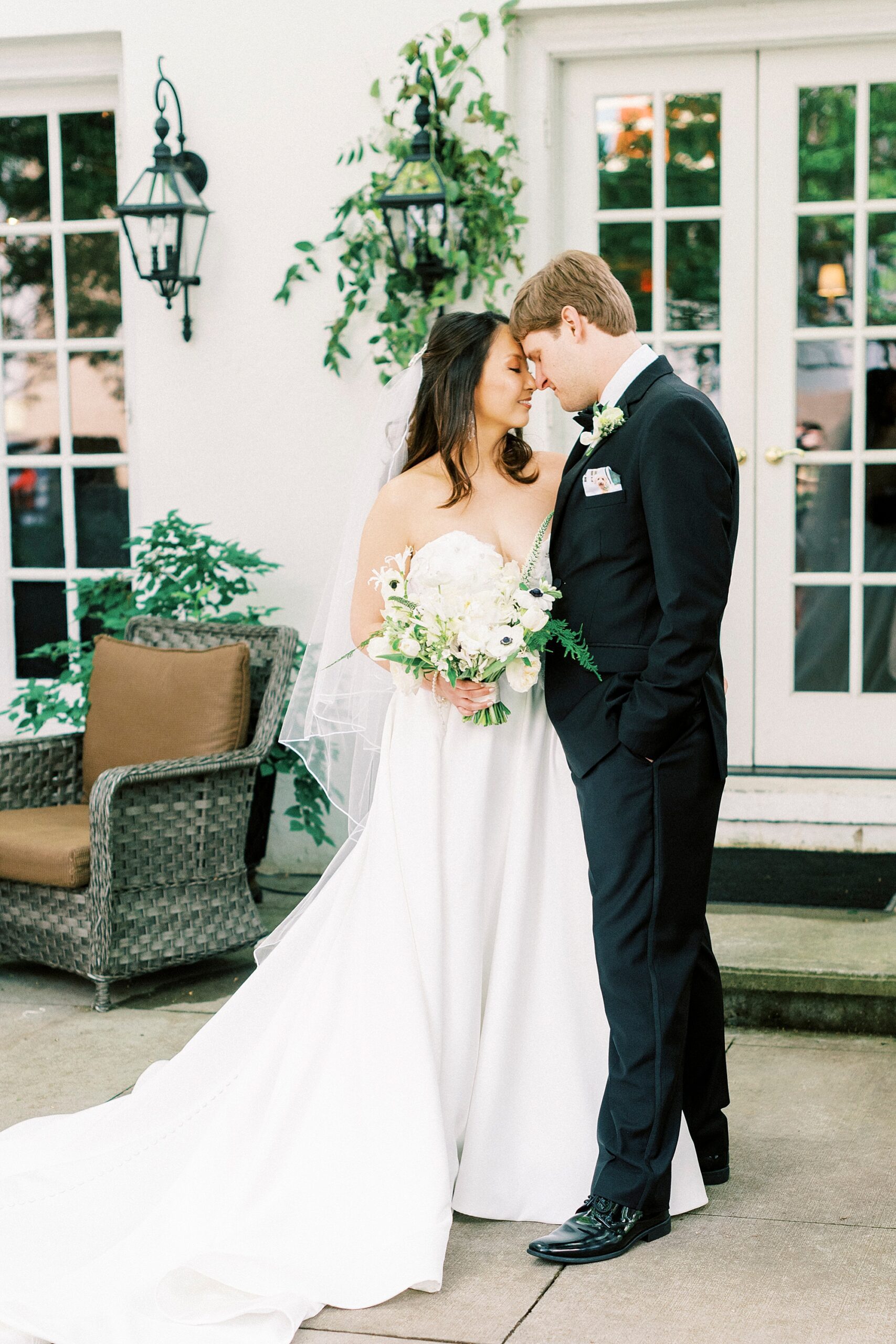 bride and groom lean heads together on patio in front of green ferns at The Spring House