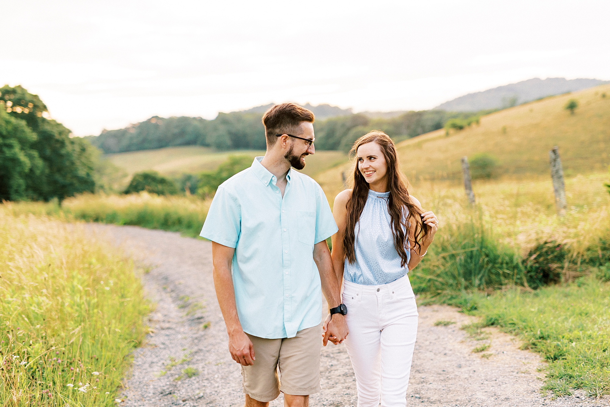 engaged couple holds hands walking down path near Moses Cone Manor