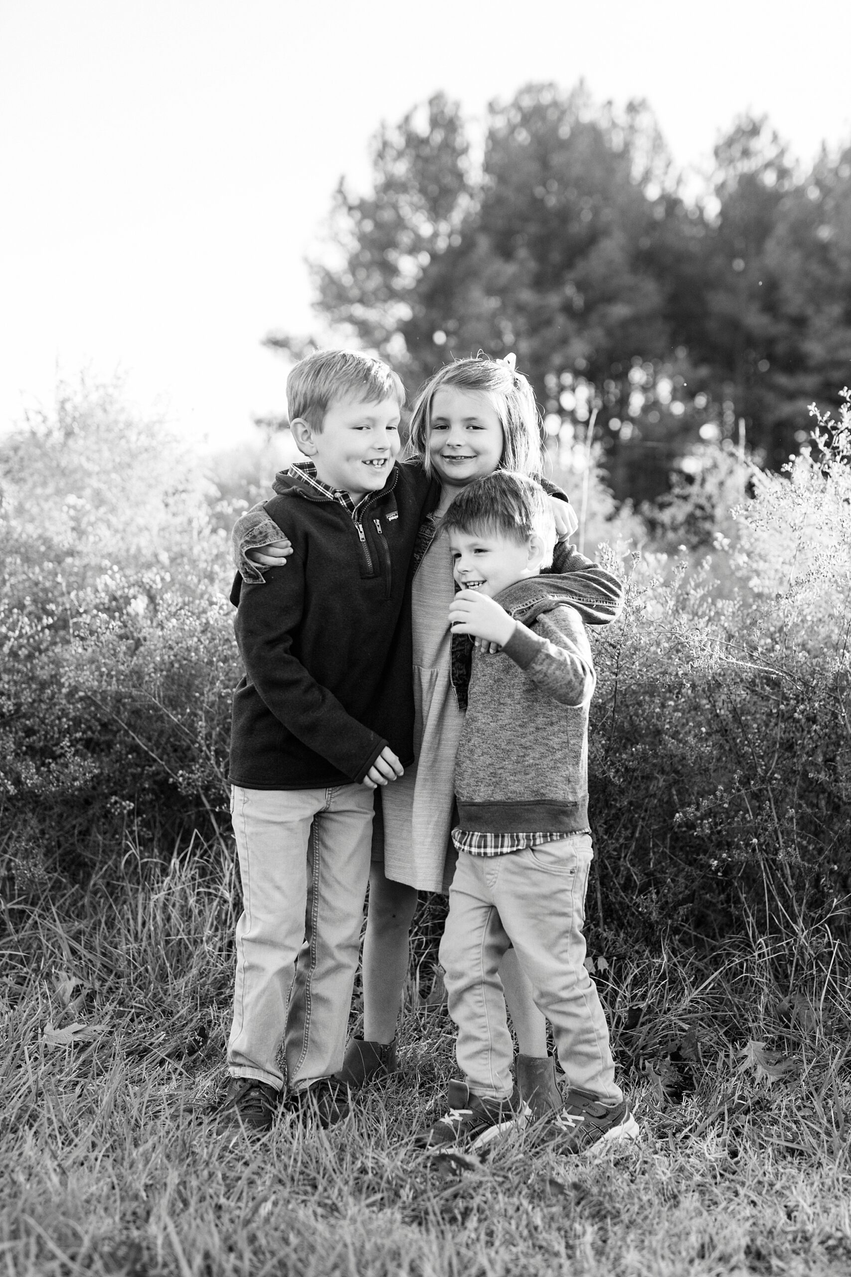 three siblings hug by tall grass in field at Frank Liske Park