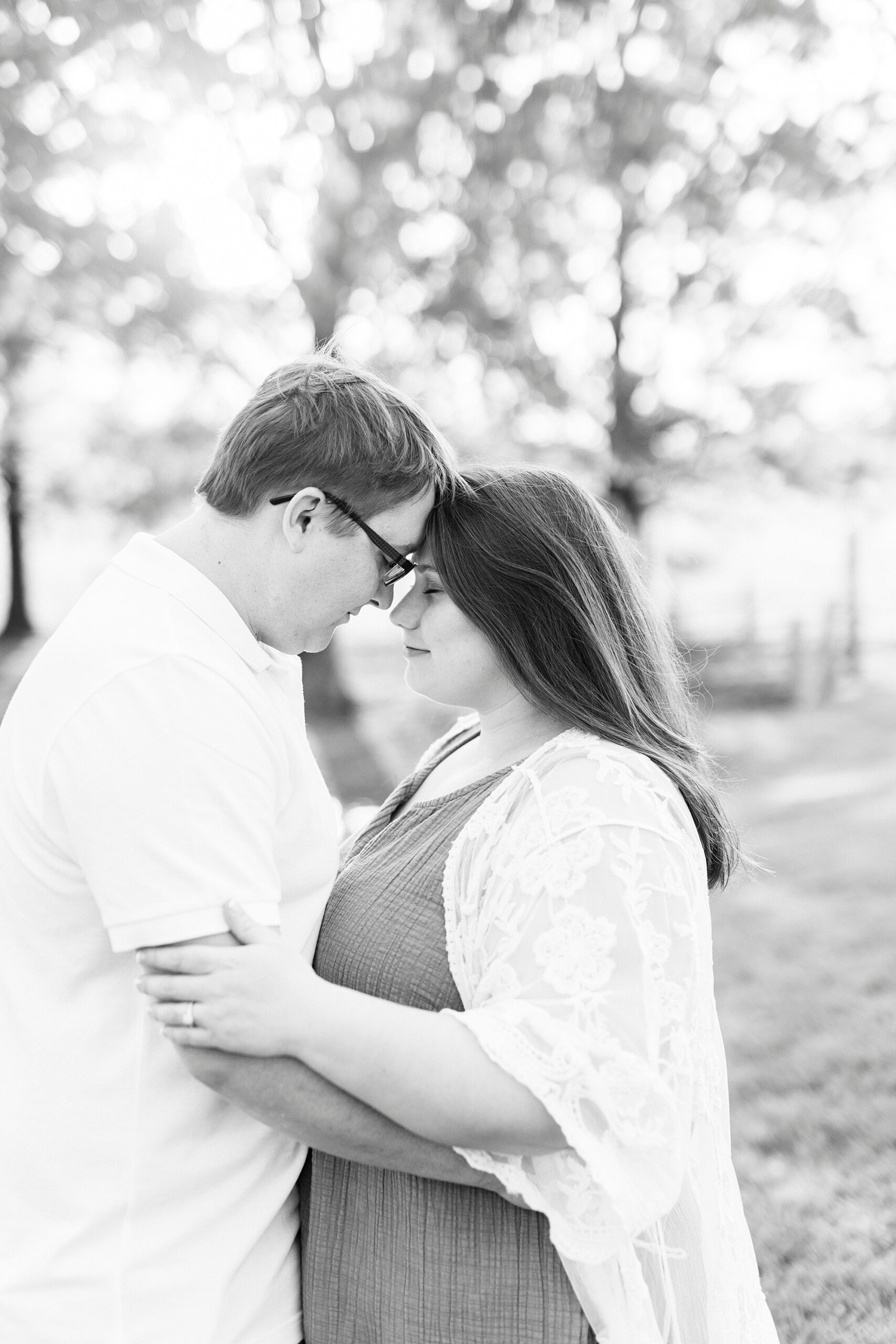 engaged couple leans heads together at sunset in trees at the Farmstead