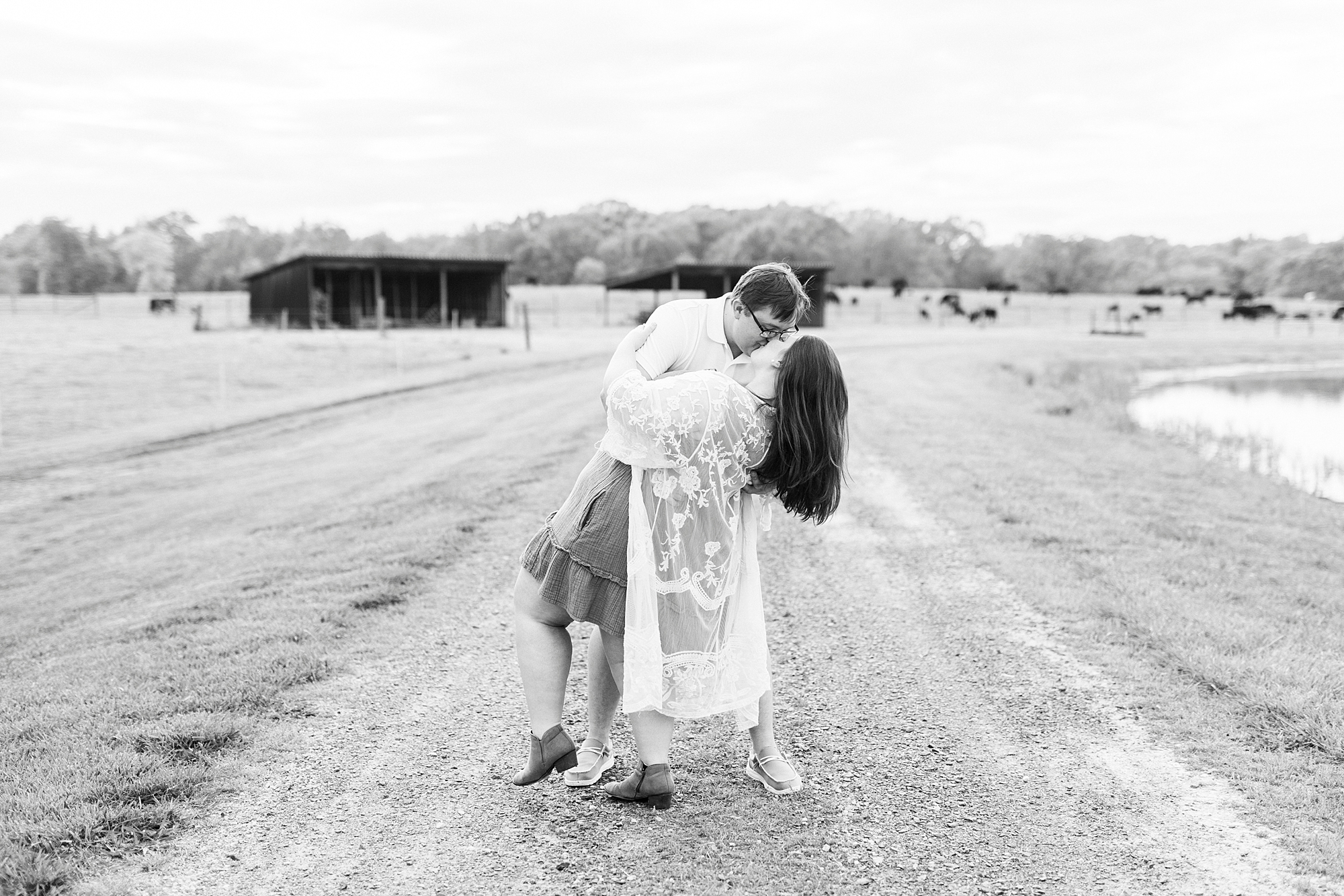 man in white polo dips fiancee on dirt path at the Farmstead