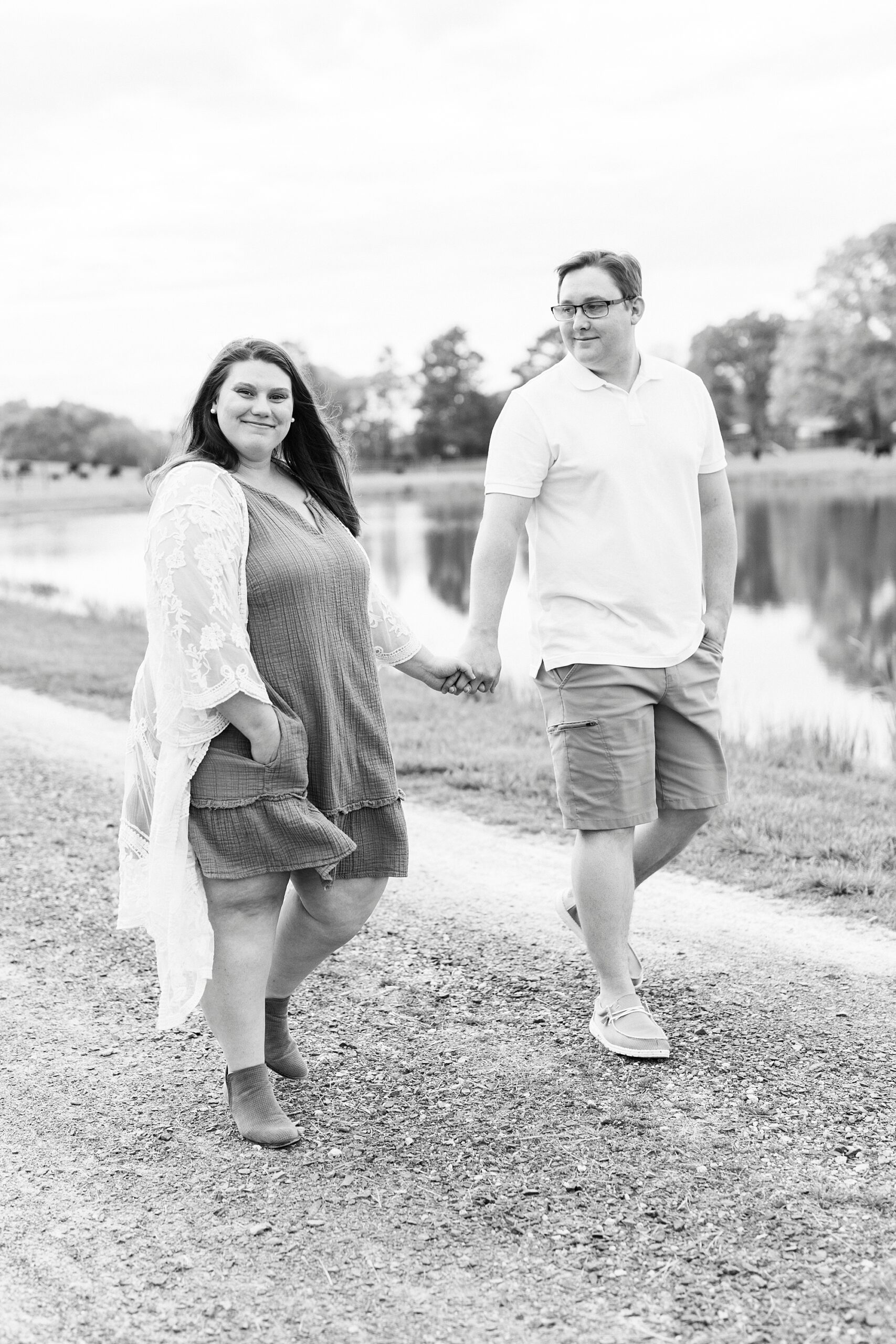 woman in dress with lace sweater walks holding man's hand by lake at the Farmstead