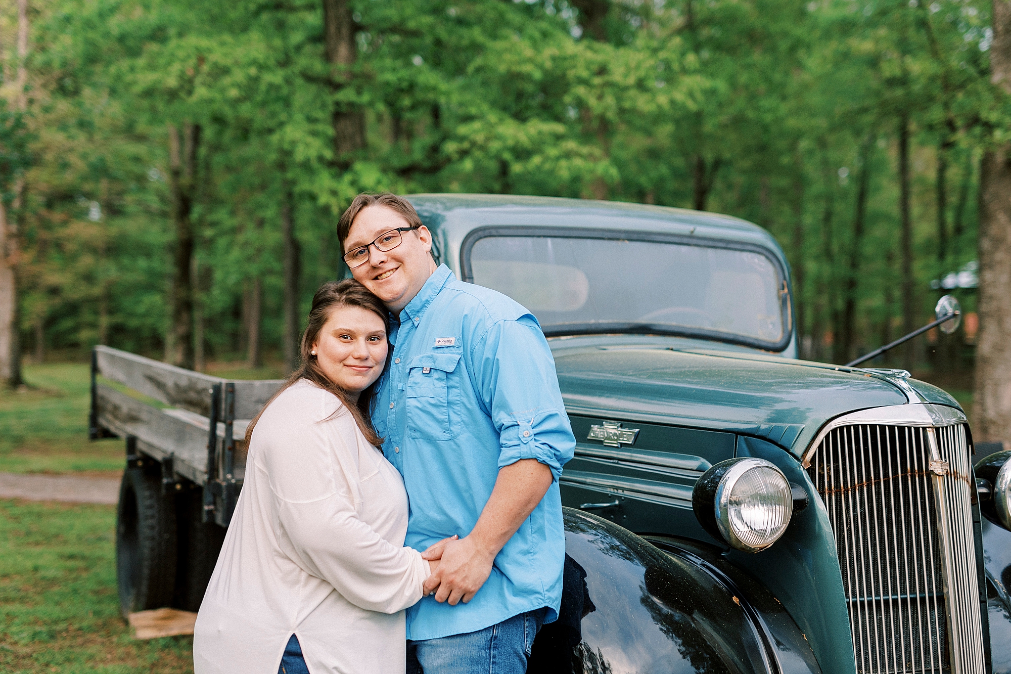engaged couple hugs near vintage teal truck