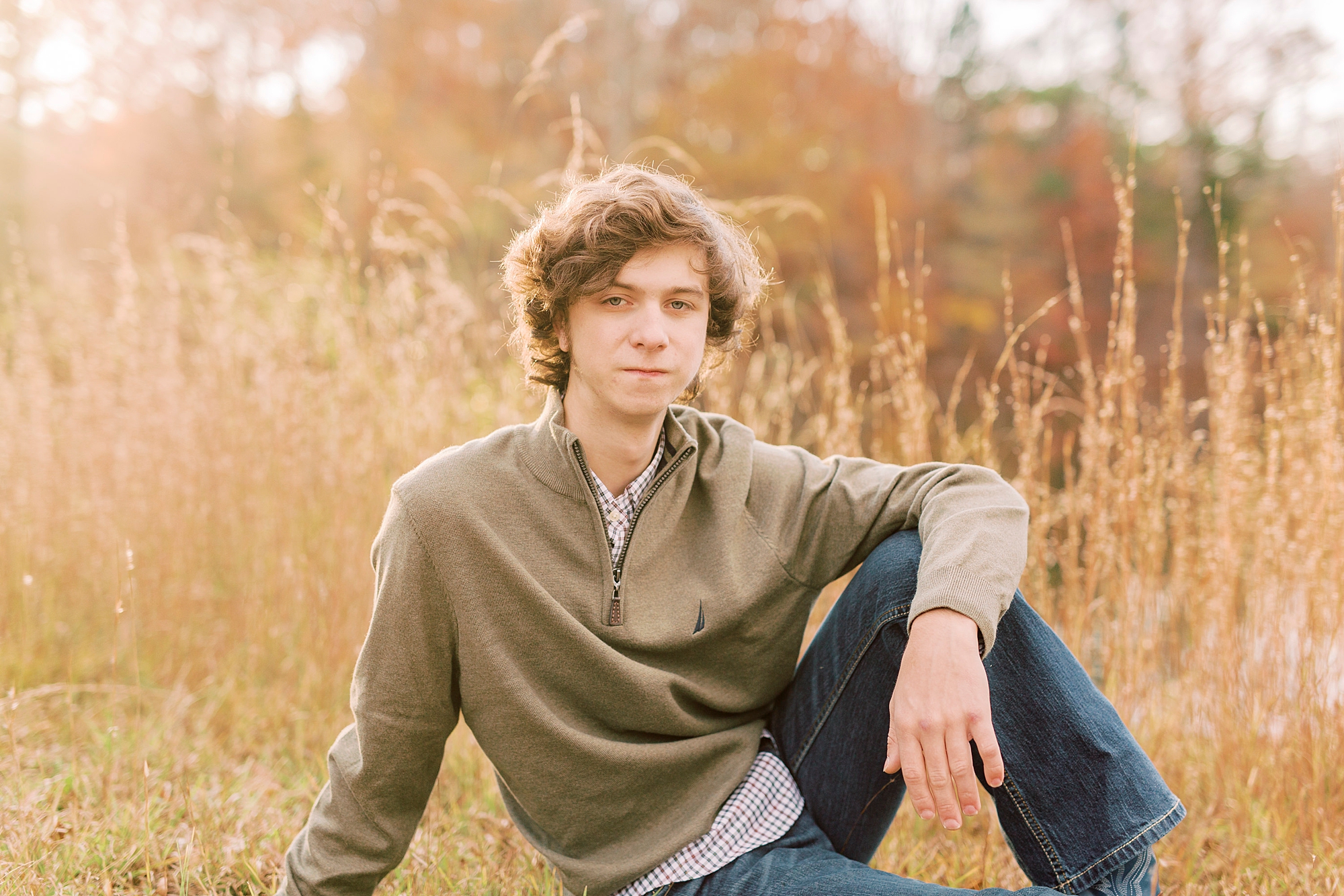 senior sits with arm falling on knee near tall grass in Midland NC