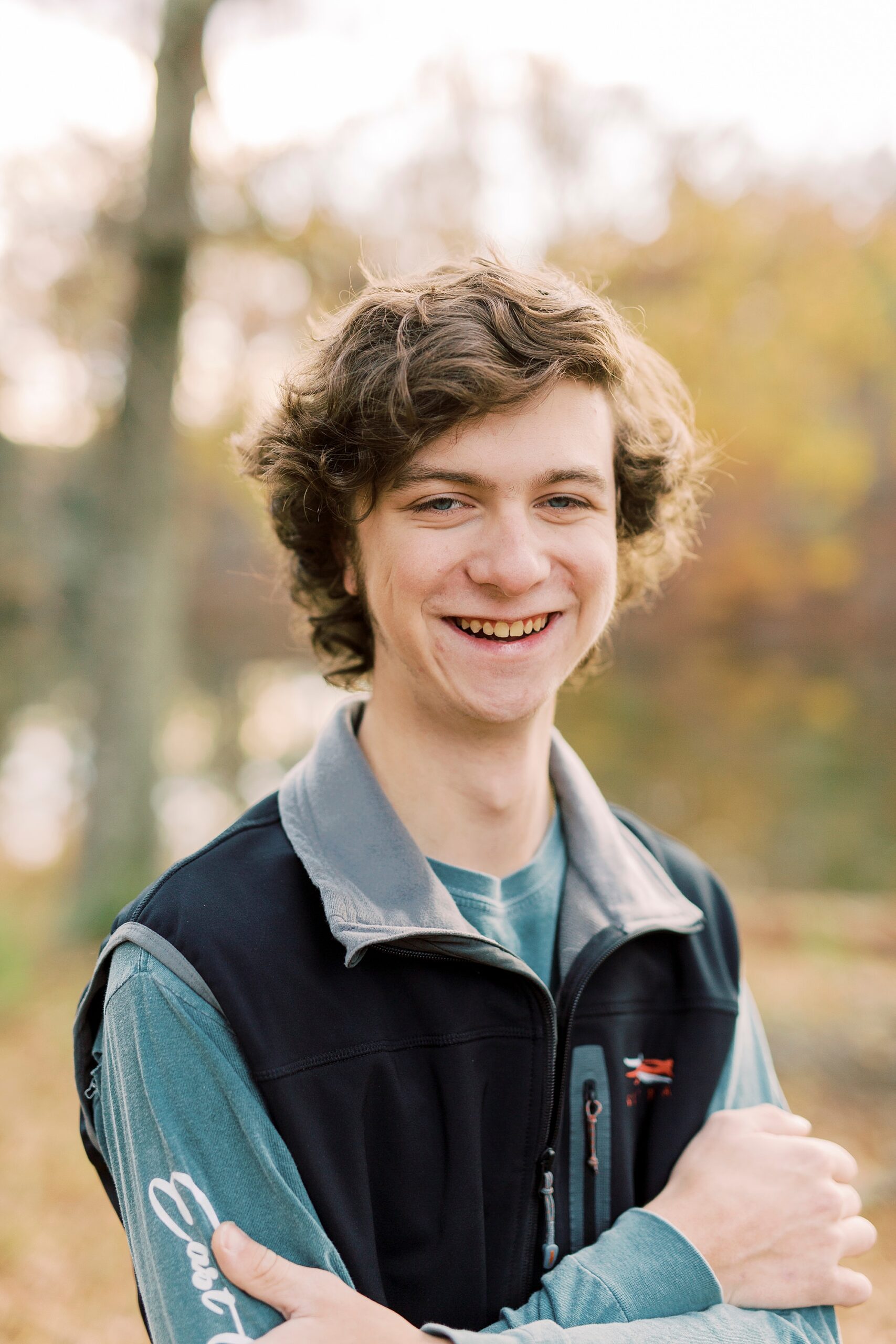 boy in black vest stands near lake during Midland NC senior portraits 