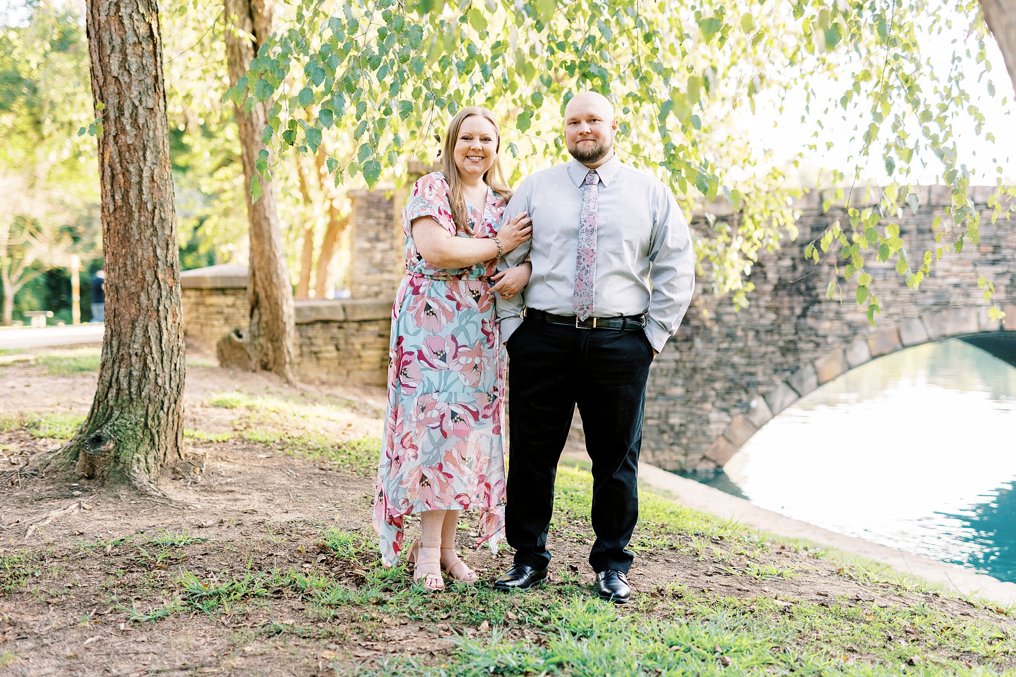 engaged couple hugs near brick bridge in Freedom Park
