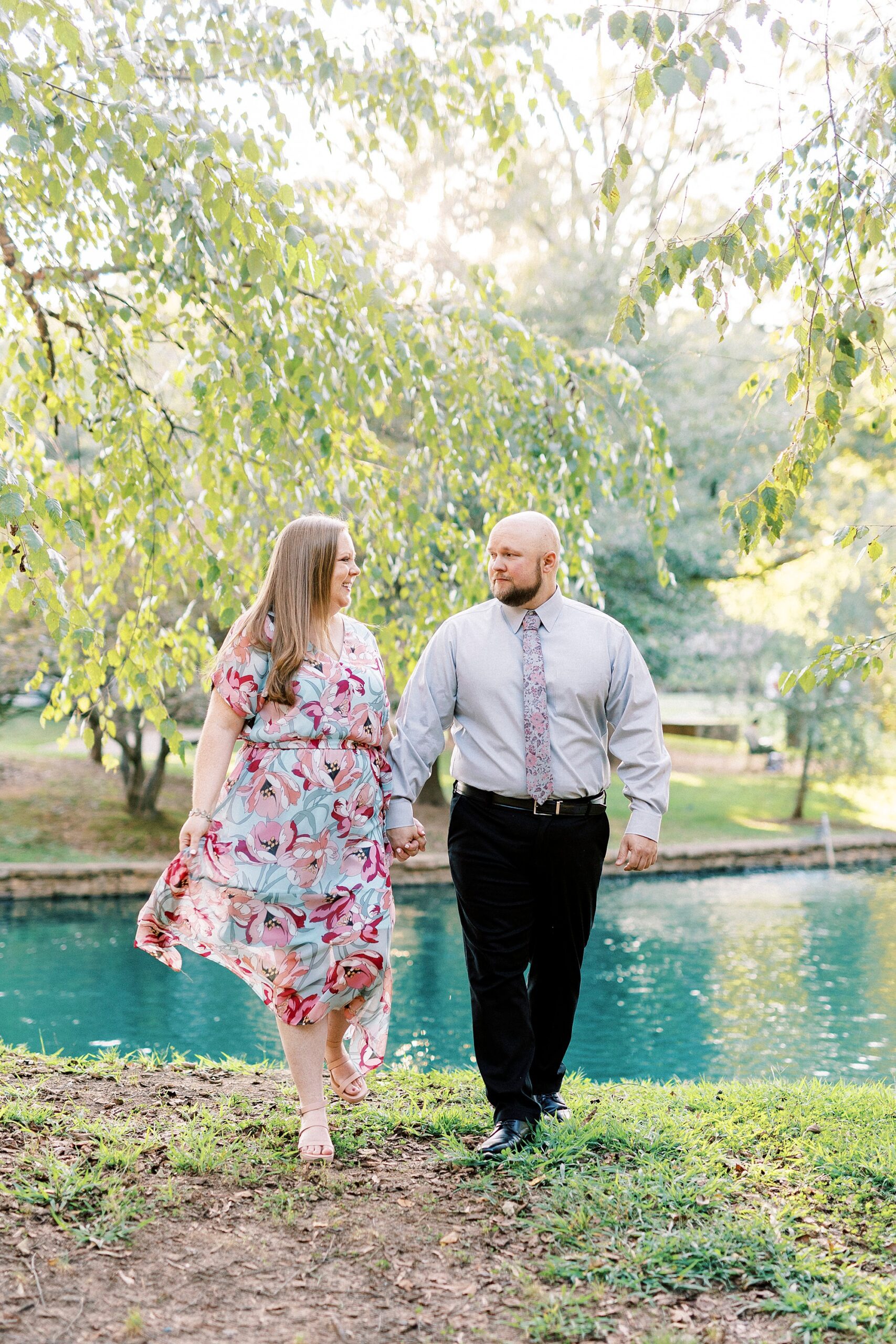 engaged couple holds hands walking near pond in Freedom Park