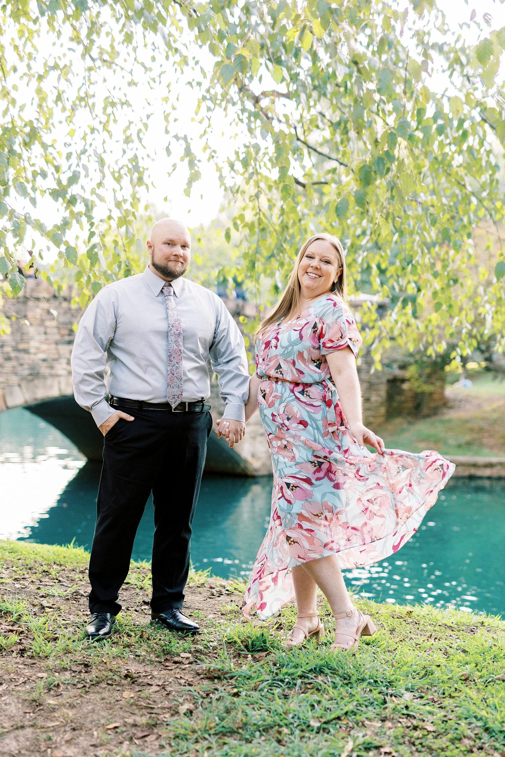 woman twirls skirt while holding fiance's hand near pond in Freedom Park
