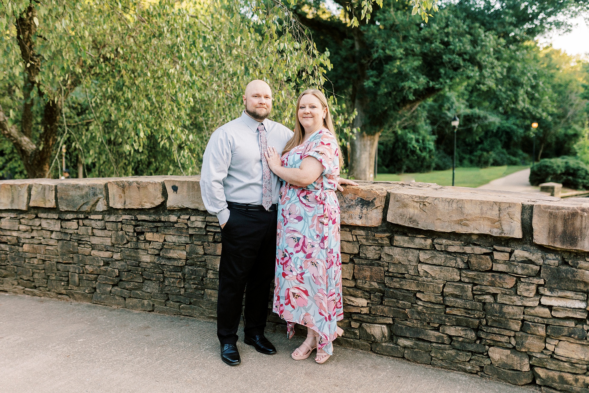 woman stands hugging man laying hand on chest on stone bridge