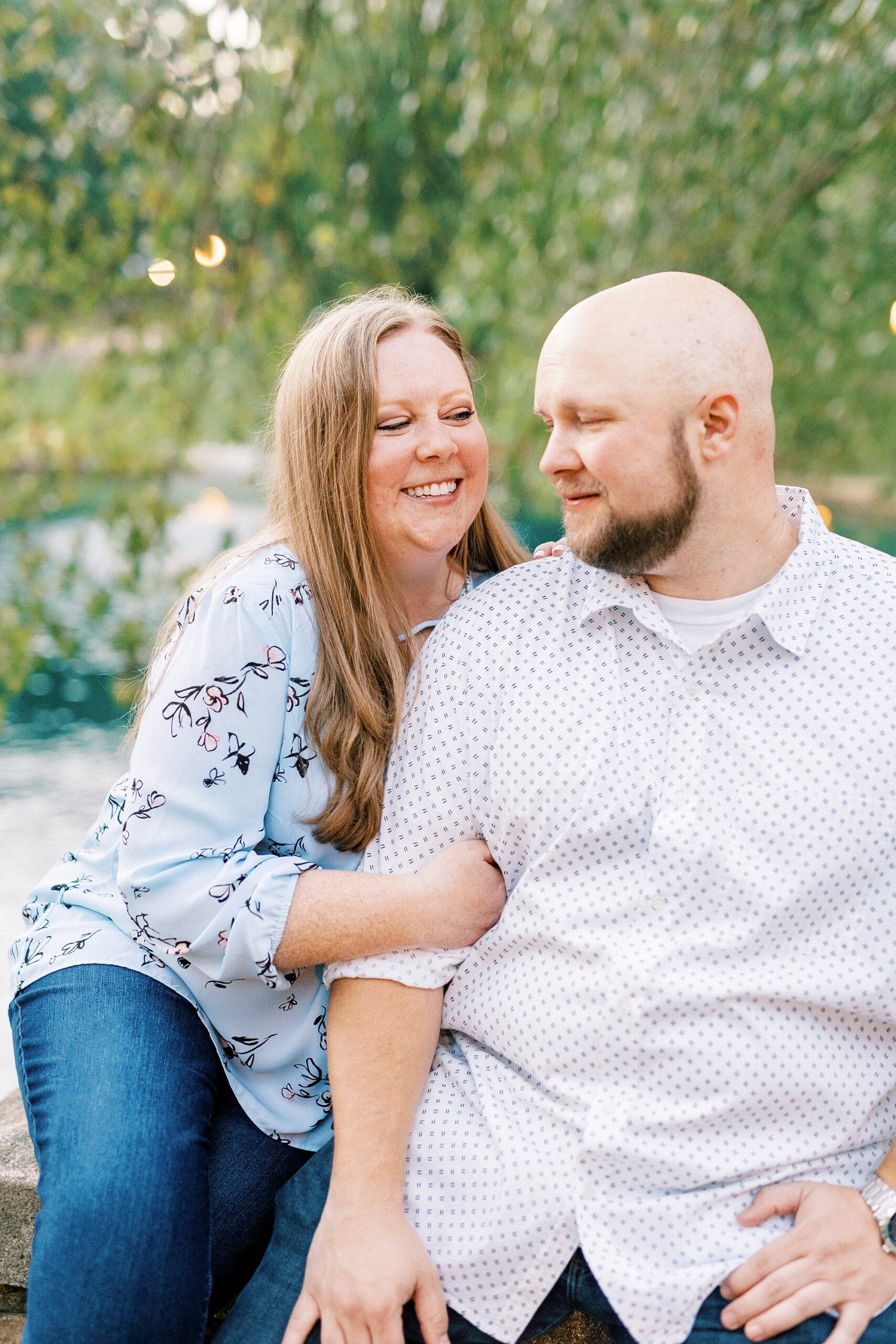 woman holds man's arm sitting on stone bridge during NC engagement photos 