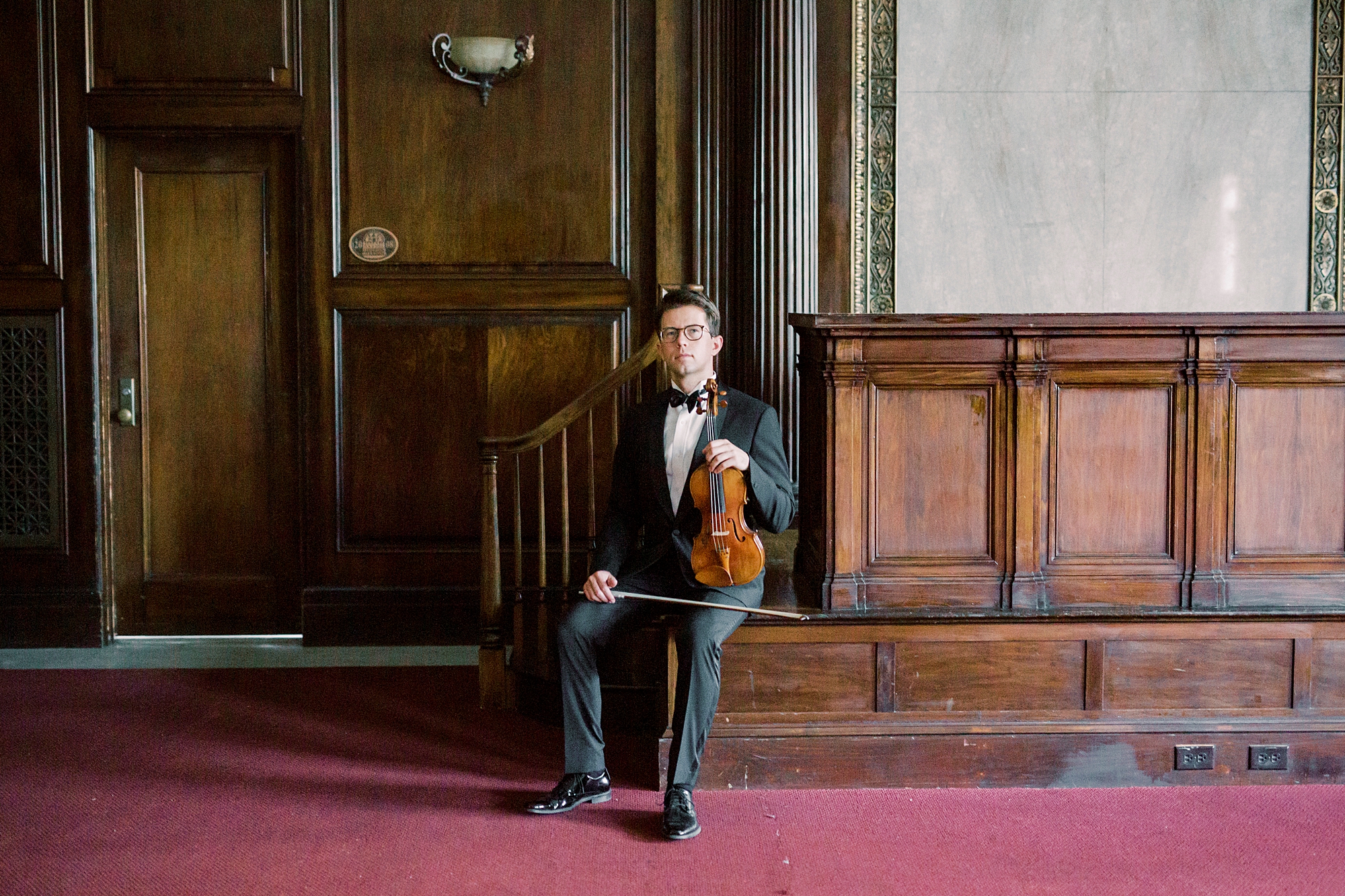 violin player in tux holds violin in his lap during headshots in South Carolina