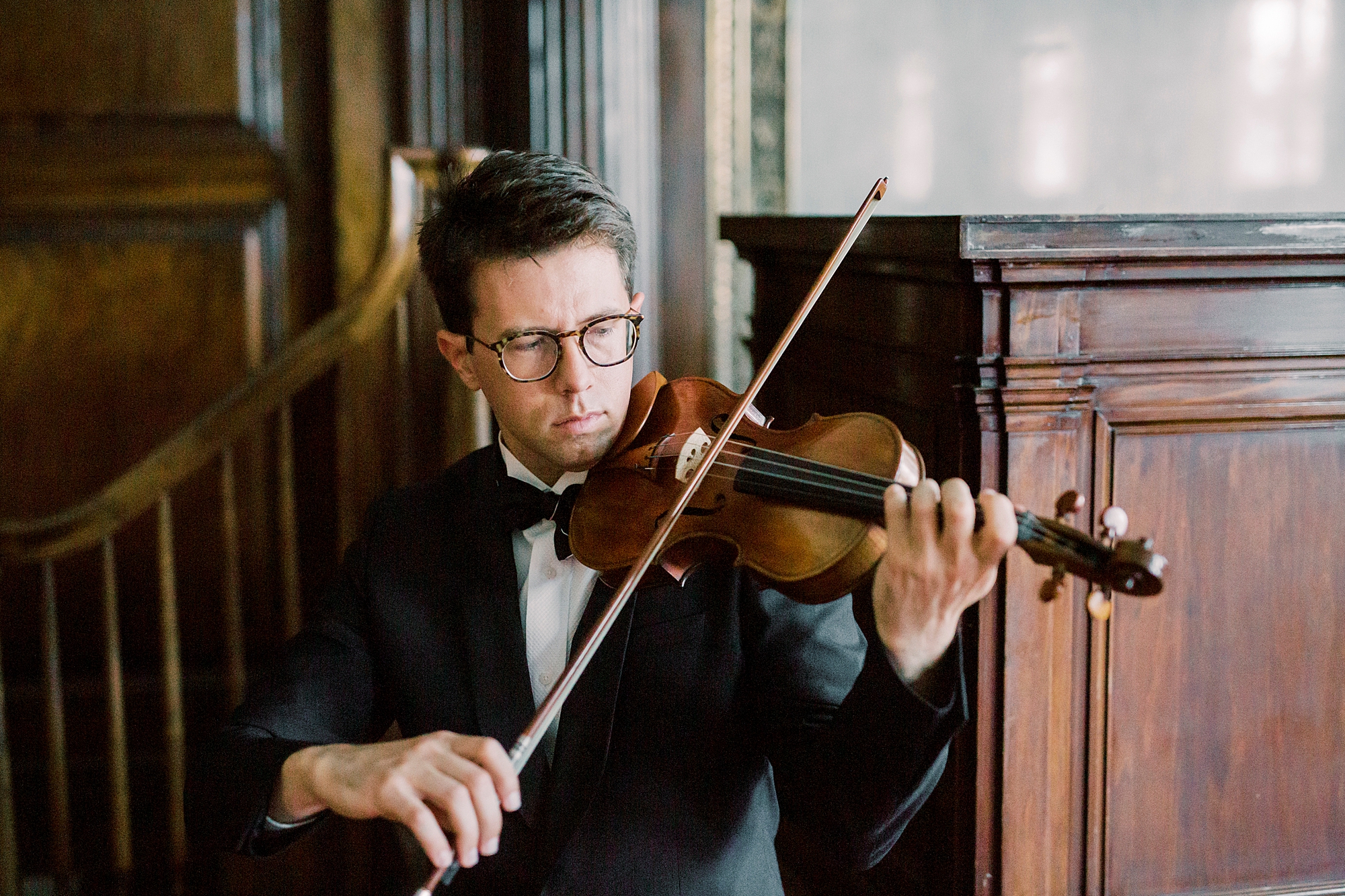violin player plays violin in front of dark wood staircase