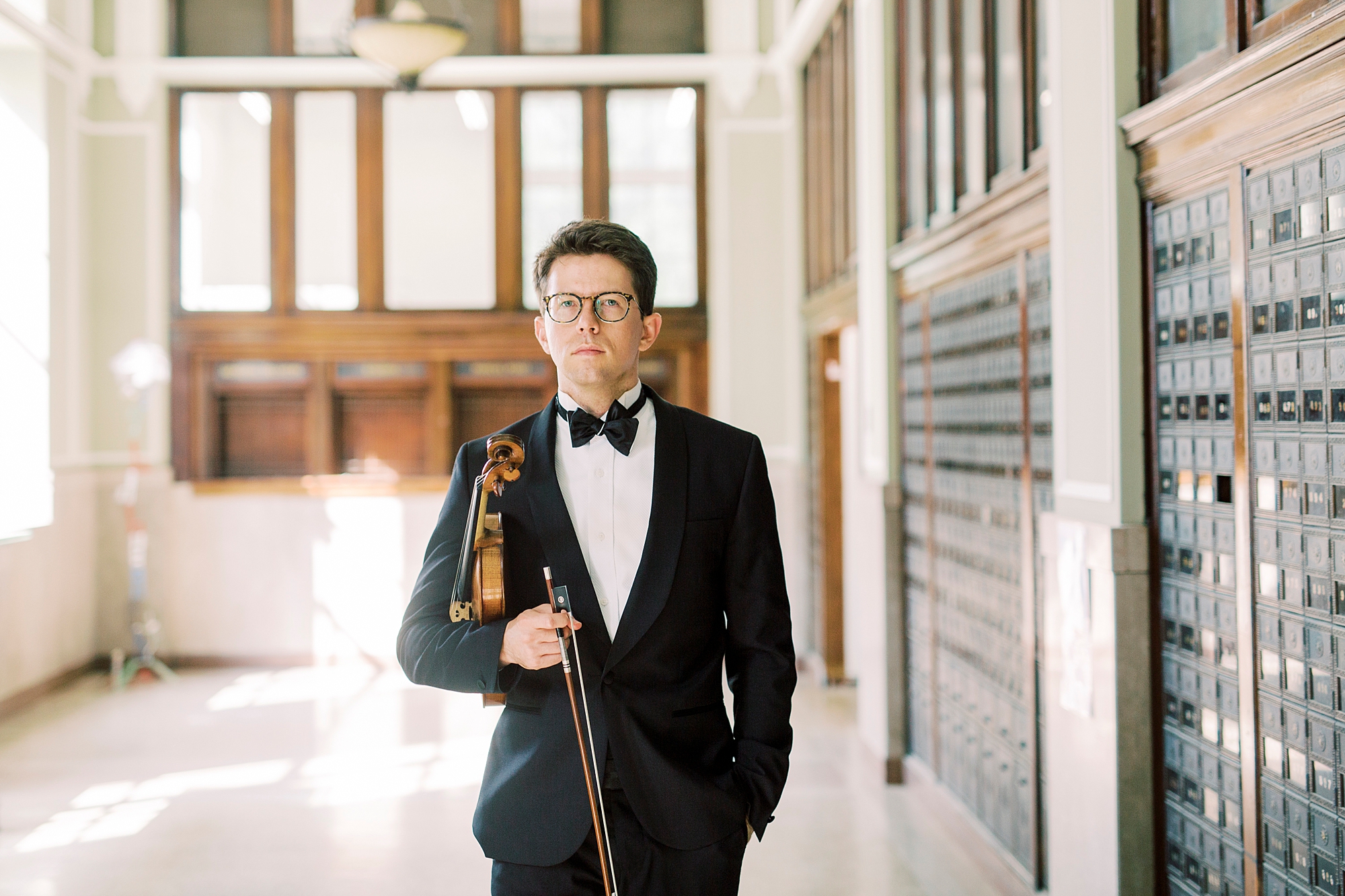 violin player in tux holds violin under his arm and holds bow in front of him