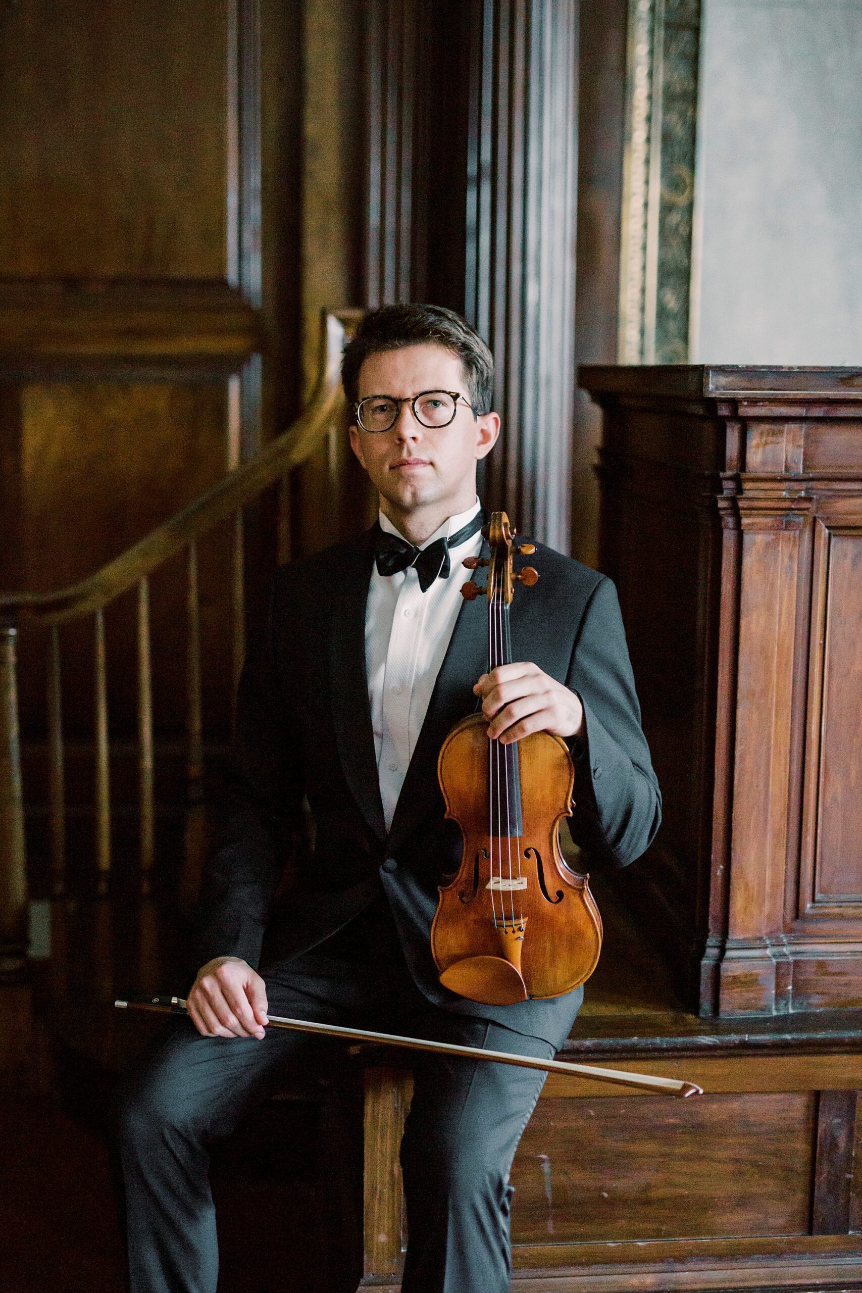 violin player sits with violin resting on leg with bow across his lap