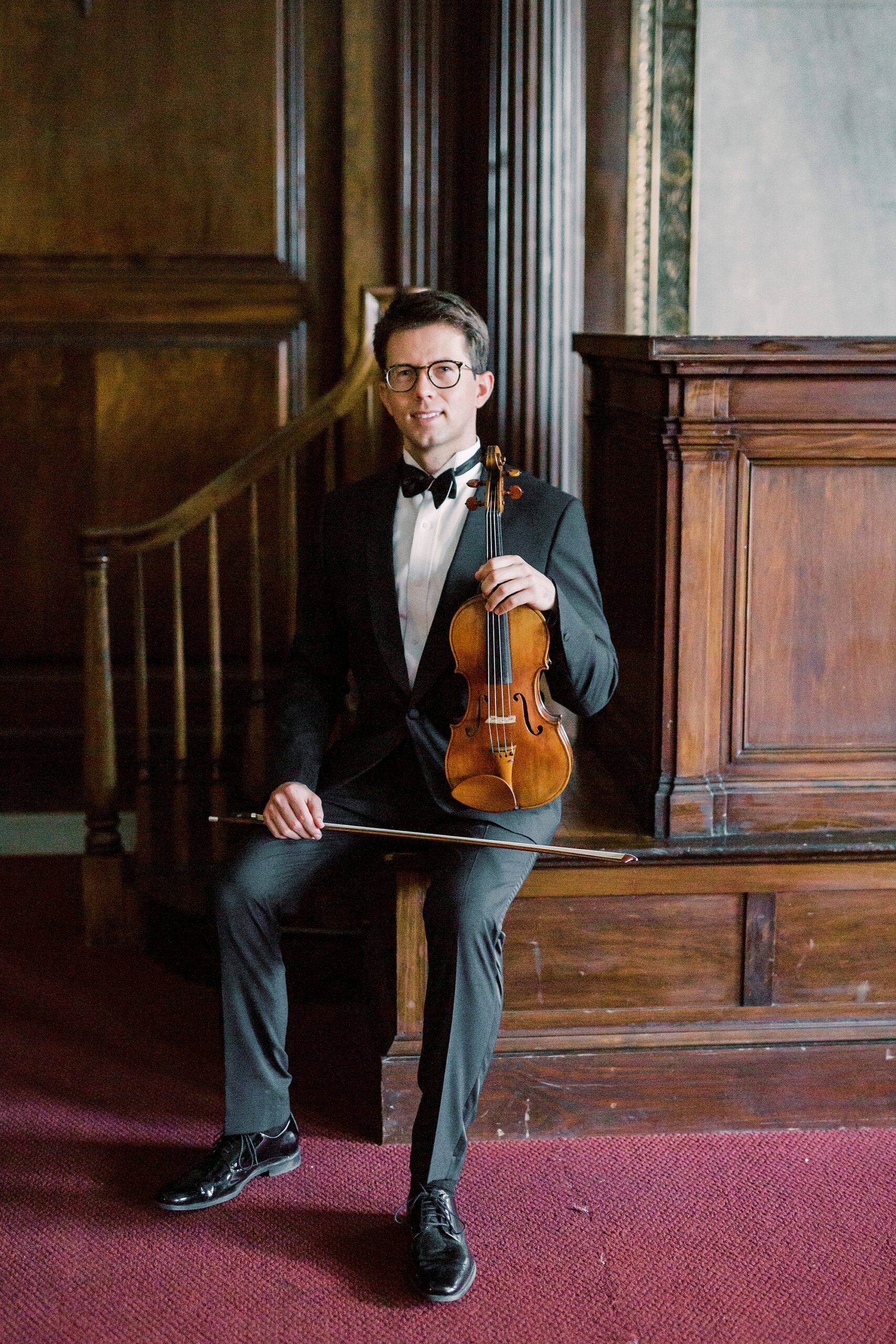 man sits holding violin during headshot session in Rock Hill SC