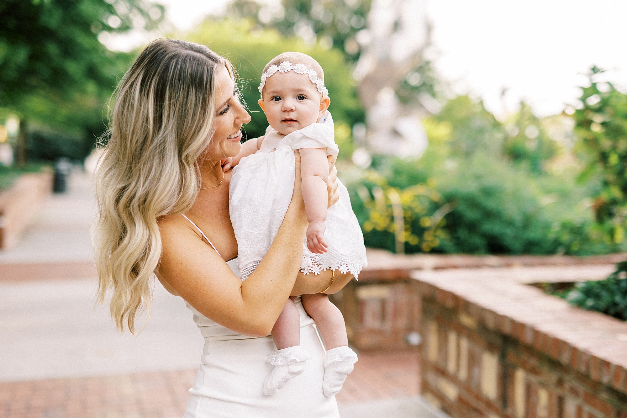 mom holds daughter in white dress standing in Charlotte NC park