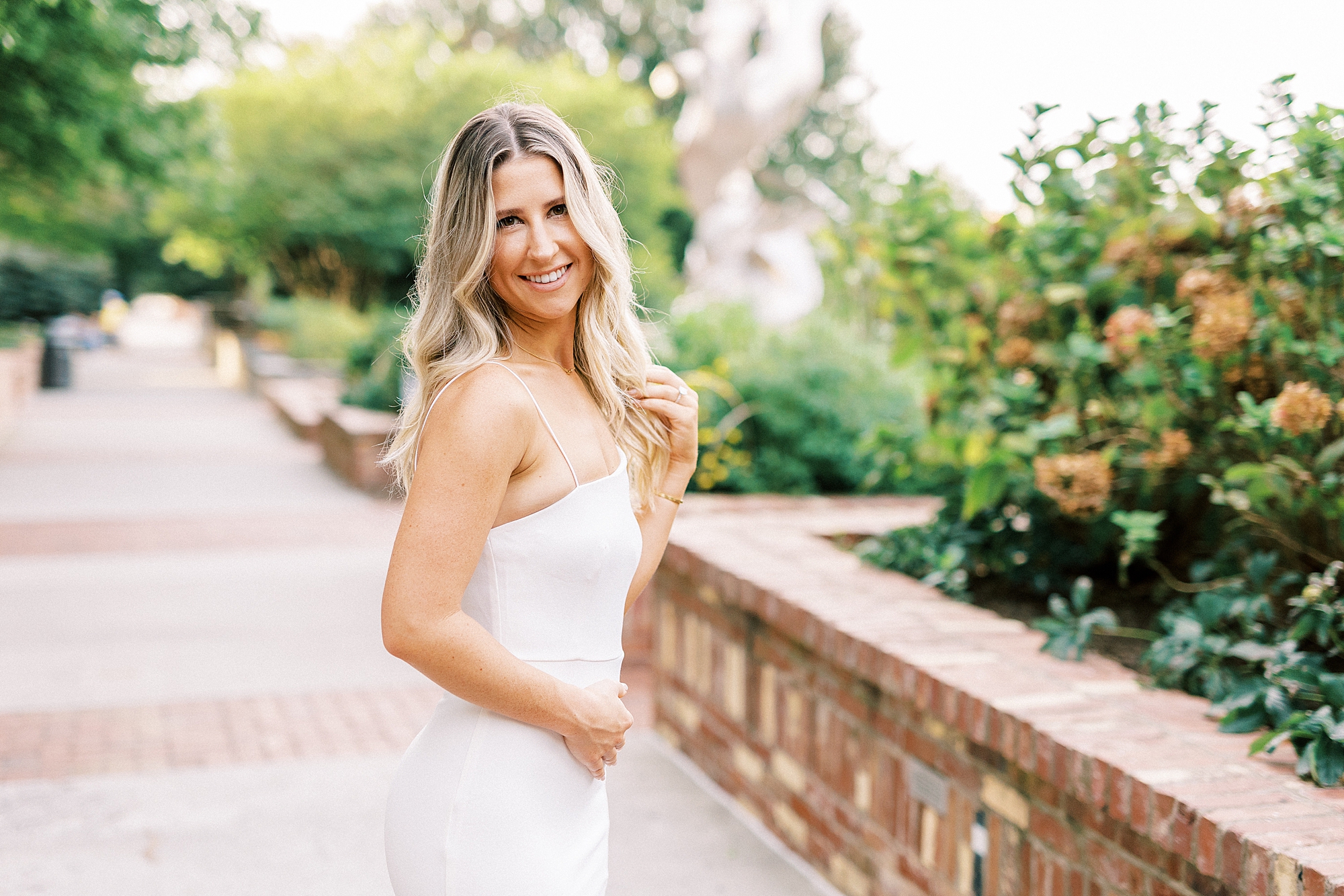 blonde woman in white dress smiles turning in park in Charlotte NC
