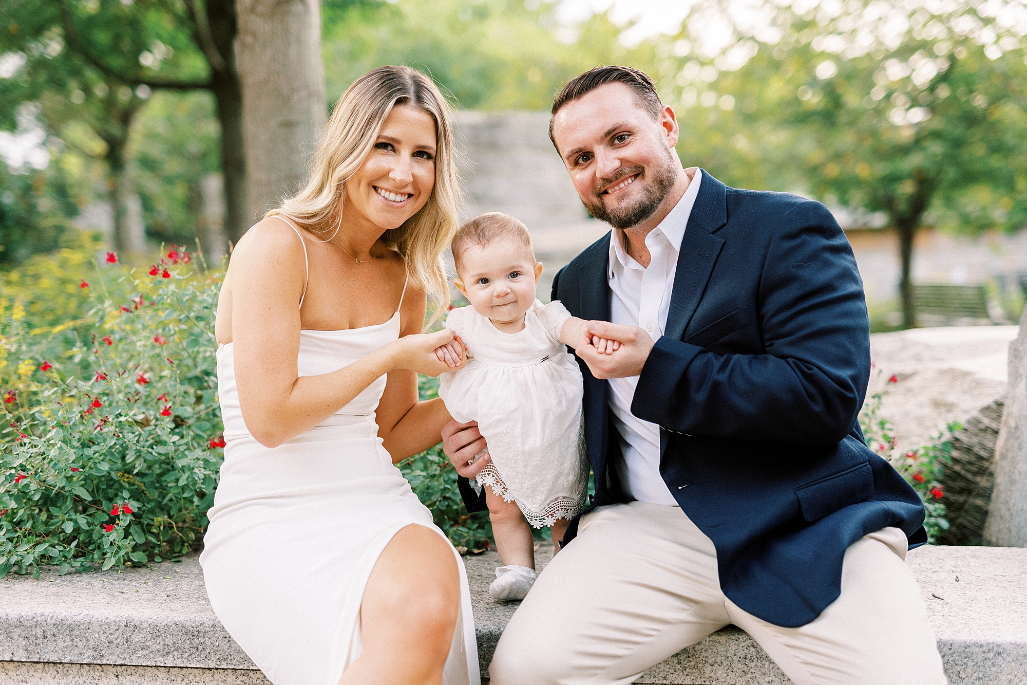 parents sit with daughter between them on rock wall during Romare Bearden Park engagement session 