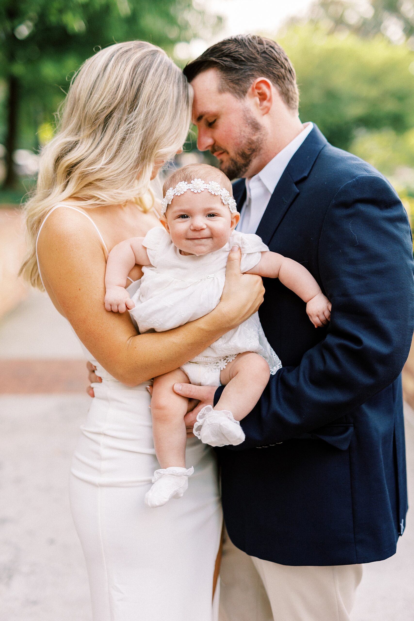 couple leans heads together holding toddler between them in Charlotte NC