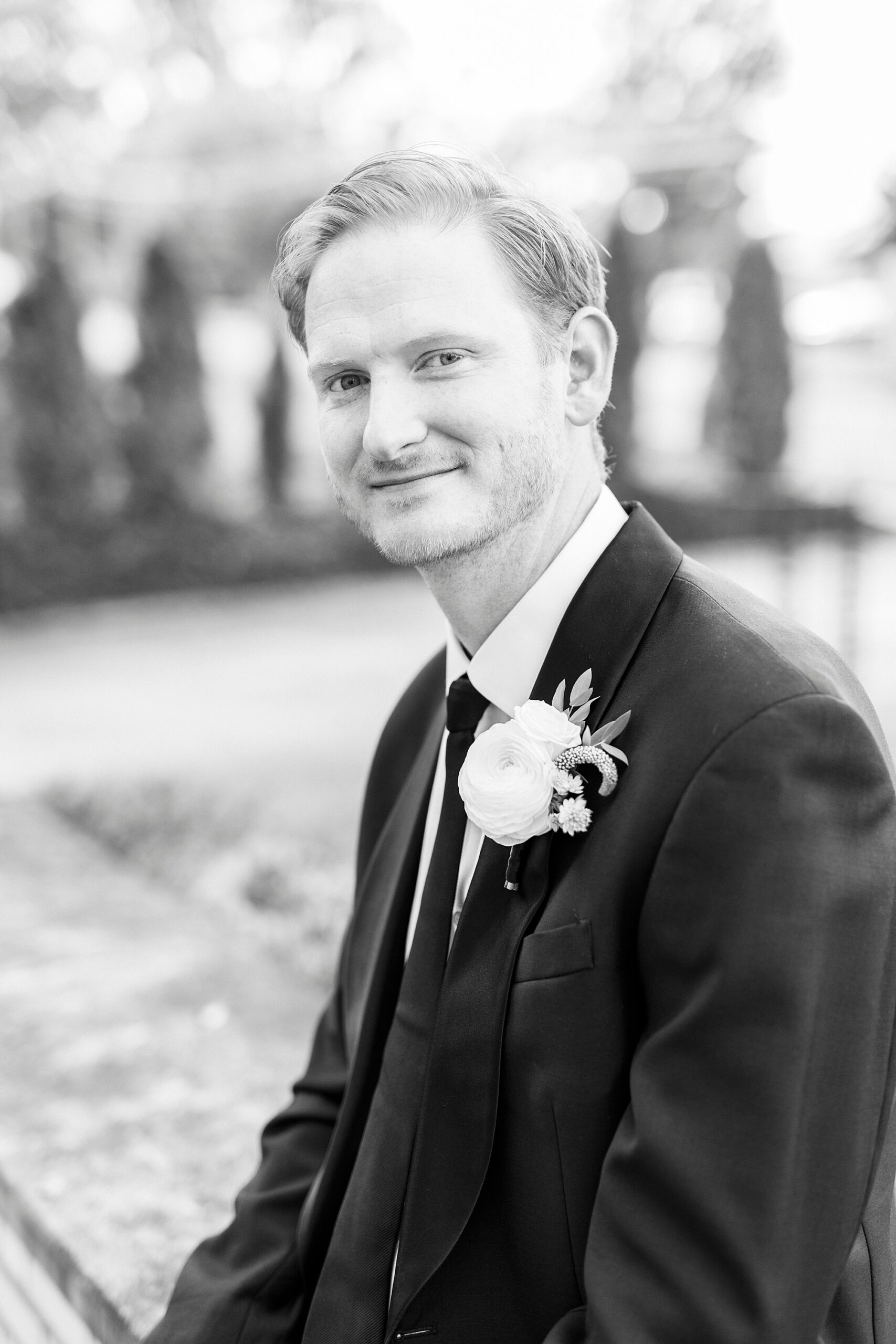 groom sits outside Separk Mansion in suit with white boutonniere 