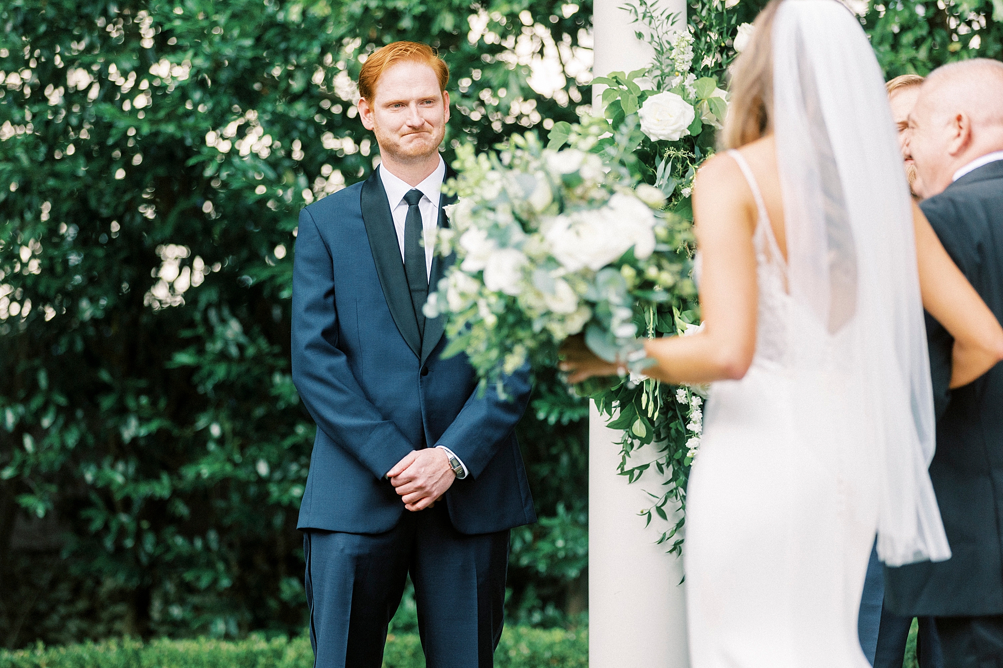 groom in navy suit looks at bride walking down aisle during outdoor wedding ceremony at Separk Mansion