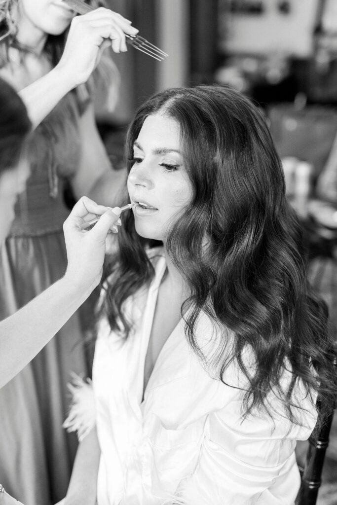 bride sits having makeup put on before fall wedding