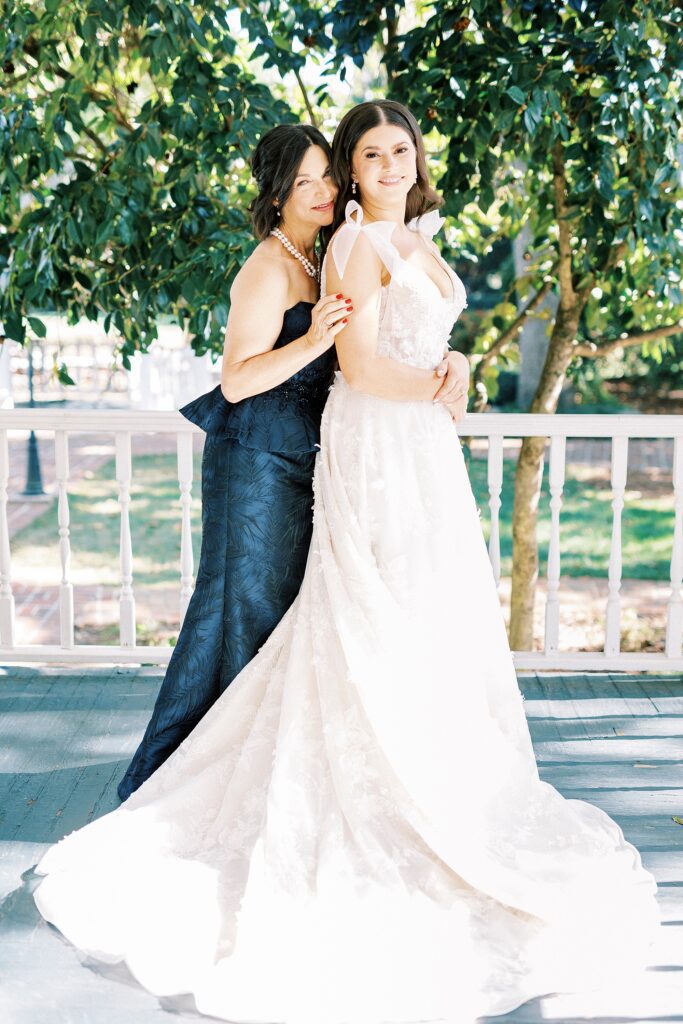mother in blue dress hugs bride on front porch of Whitehead Manor
