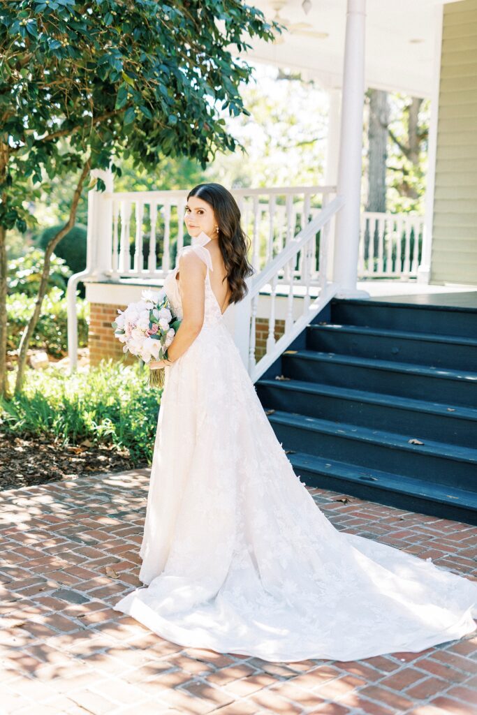bride looks over shoulder showing off wedding gown in front of Whitehead Manor