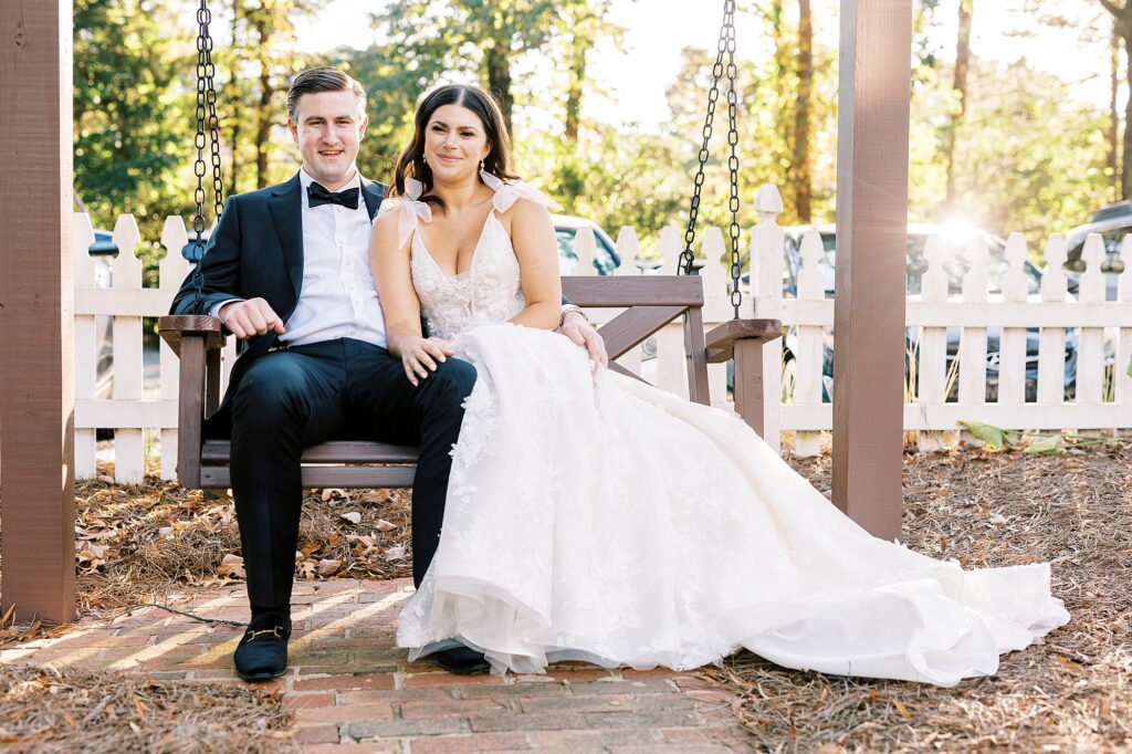 bride and groom sit on wooden bench in garden at Whitehead Manor