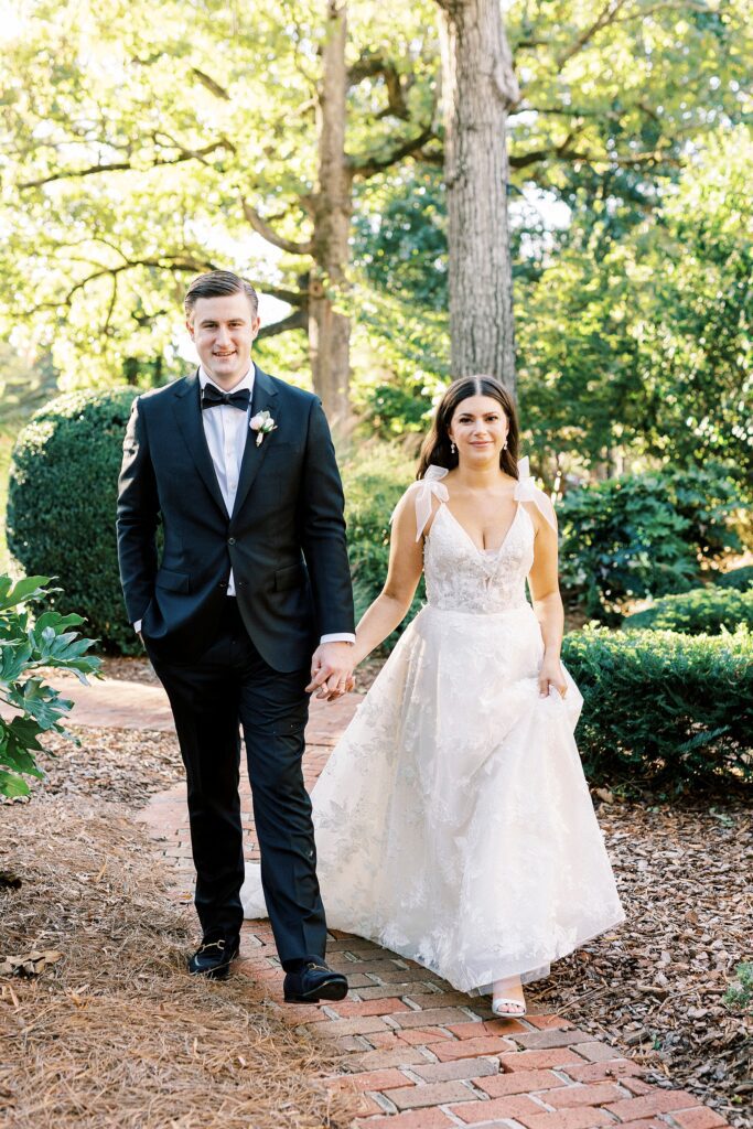 newlyweds hold hands walking across lawn at Whitehead Manor