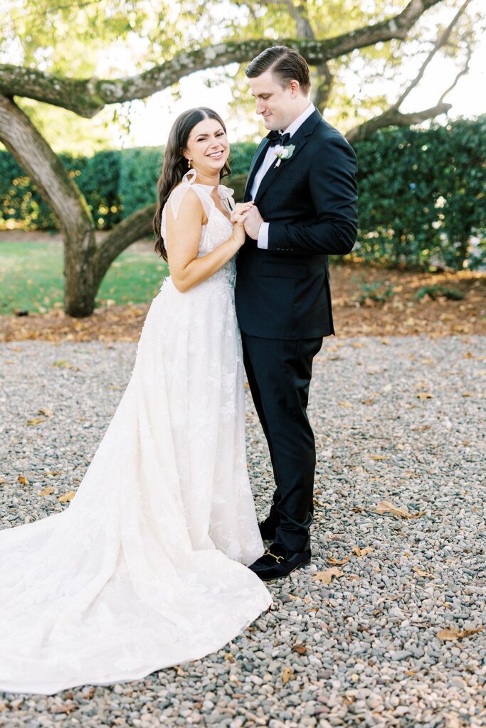 bride and groom hug holding hands near oak tree at Whitehead Manor