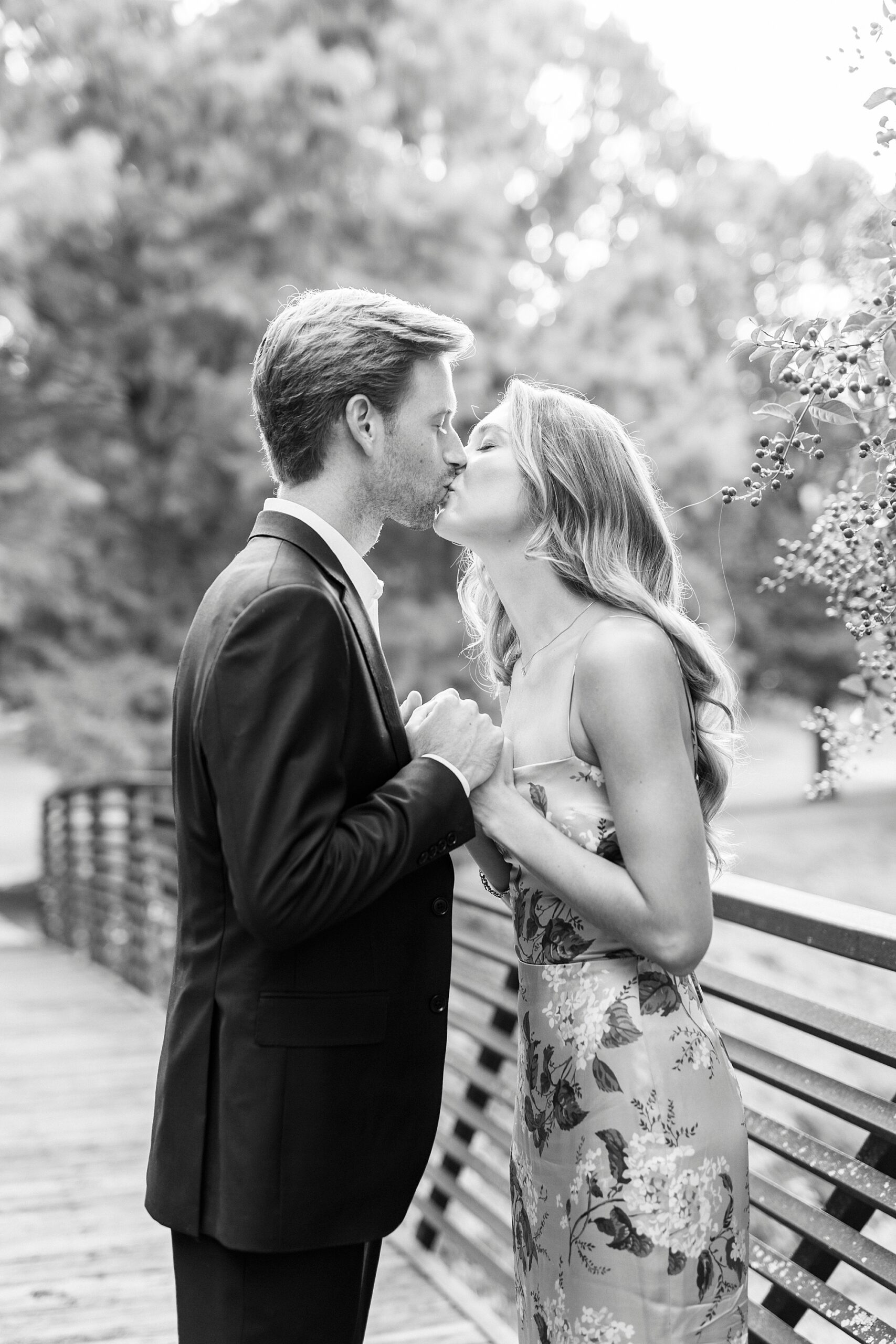 engaged couple kisses leaning against railing of bridge in Glencairn Garden