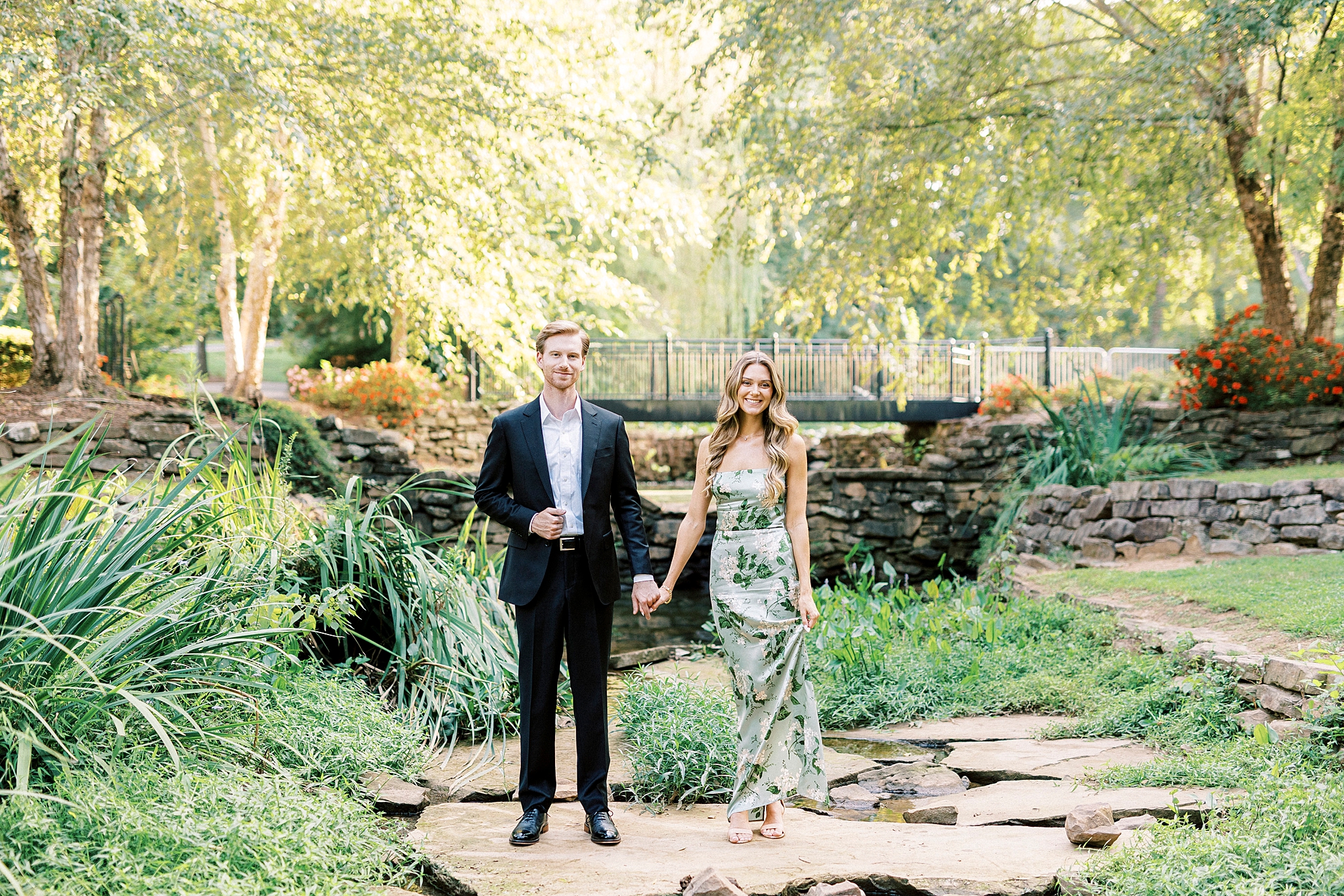 couple holds hands standing on rocks in pond at Glencairn Garden