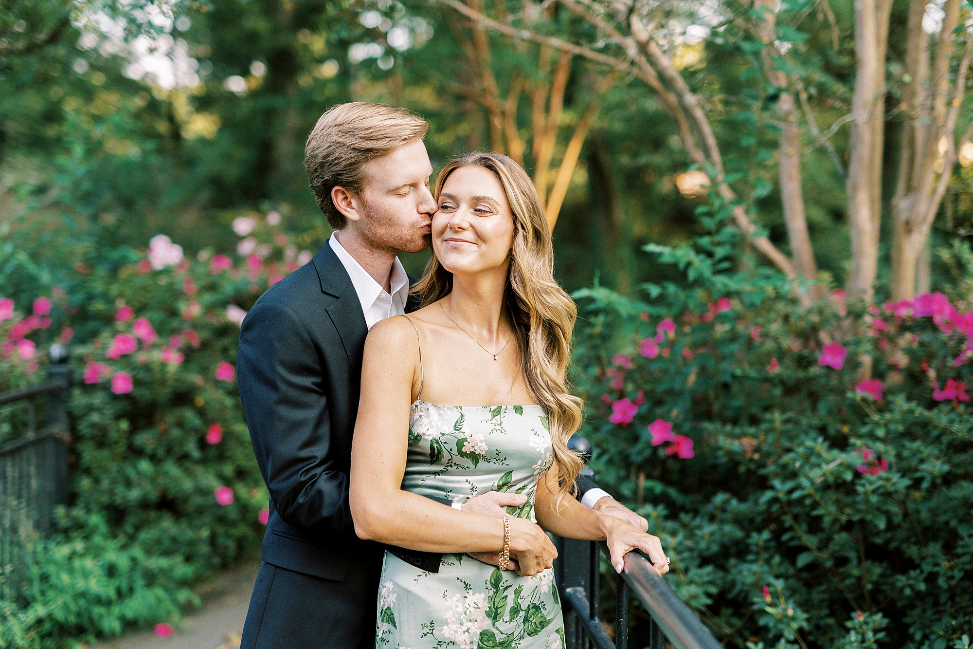 man kisses woman's cheek from behind during spring engagement session in Glencairn Garden