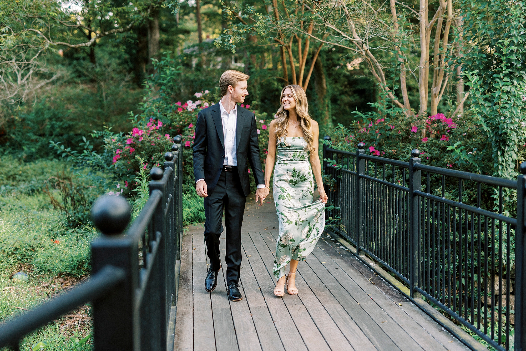 woman walks with man on bridge holding skirt of floral dress