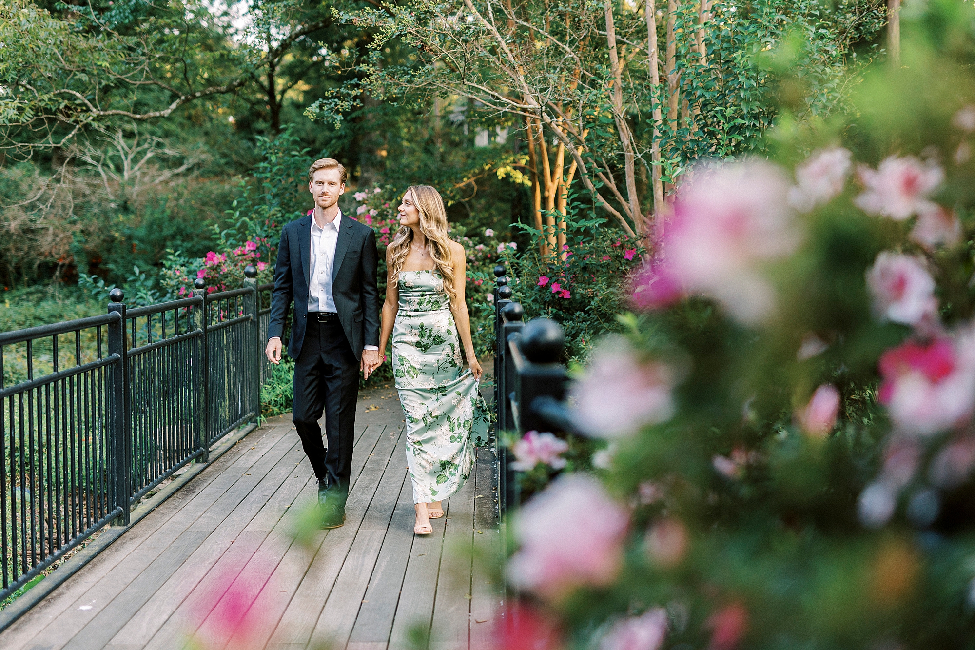 engaged couple holds hands walking on bridge in Glencairn Garden in Rock Hill SC