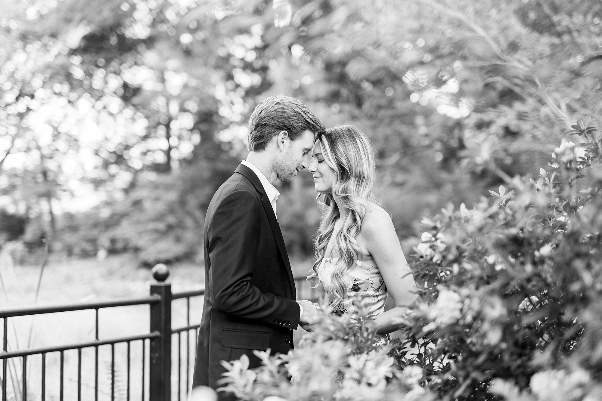 couple leans heads together near iron fence inside Glencairn Garden