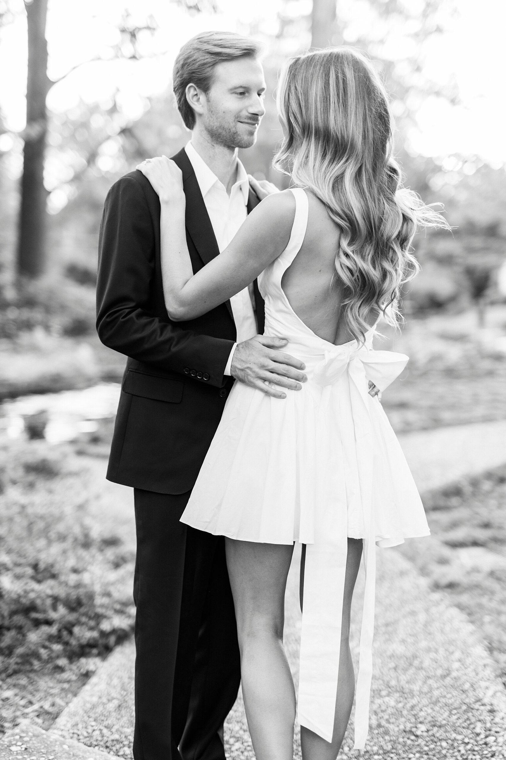 man in suit hugs woman in white dress with bow on back of dress