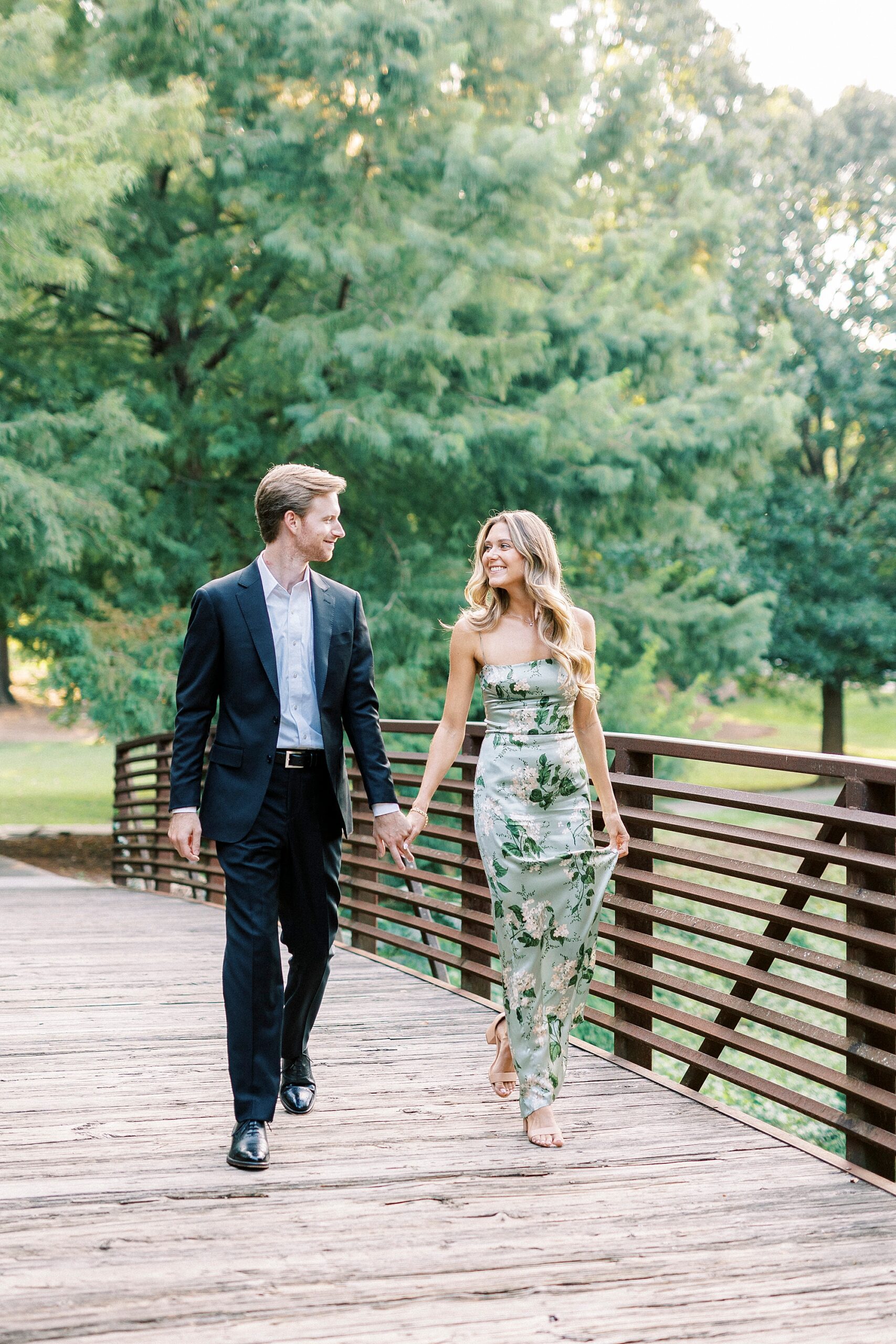 couple holds hands walking across bridge in Glencairn Garden