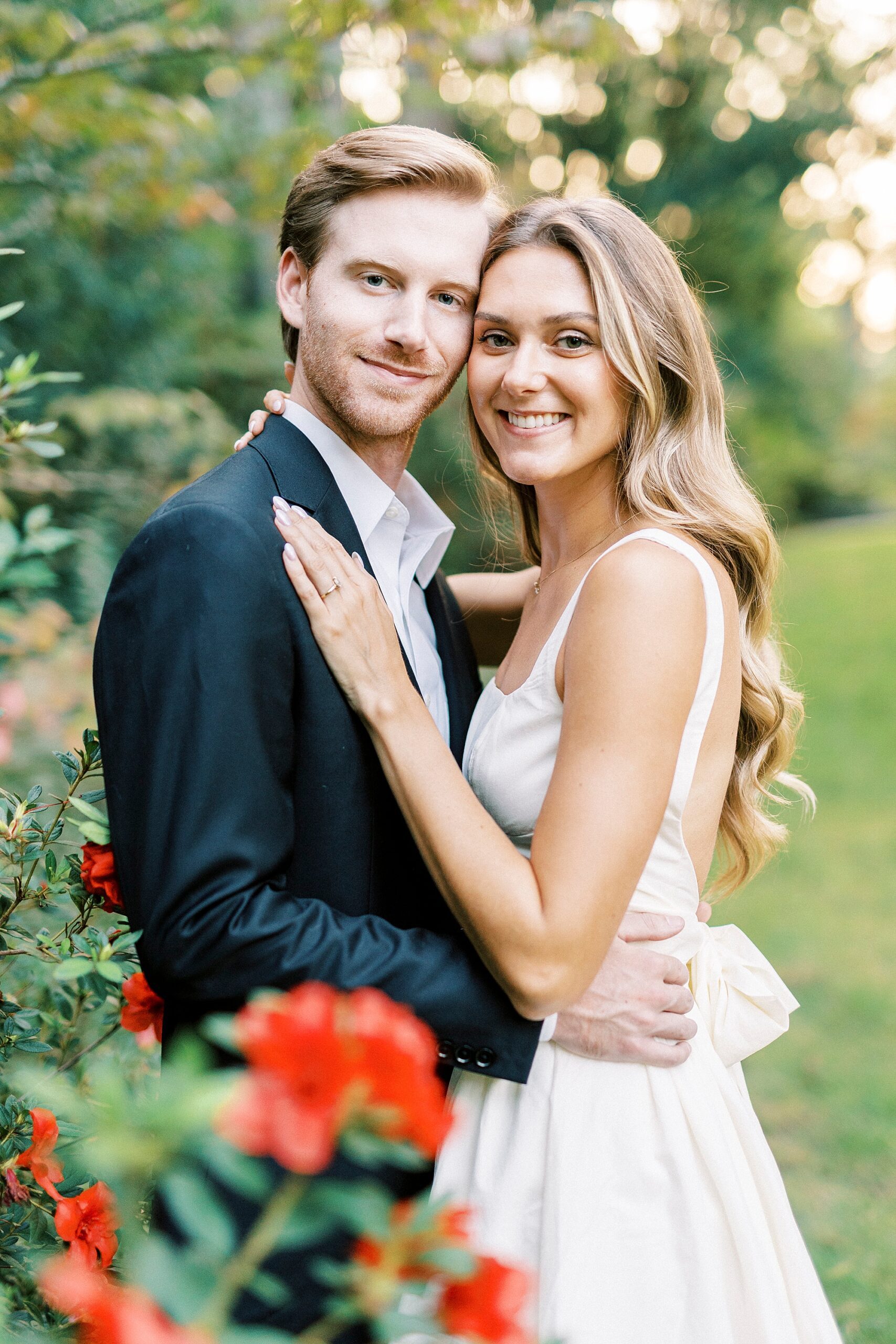 engaged couple hugs by red flowers inside Glencairn Garden