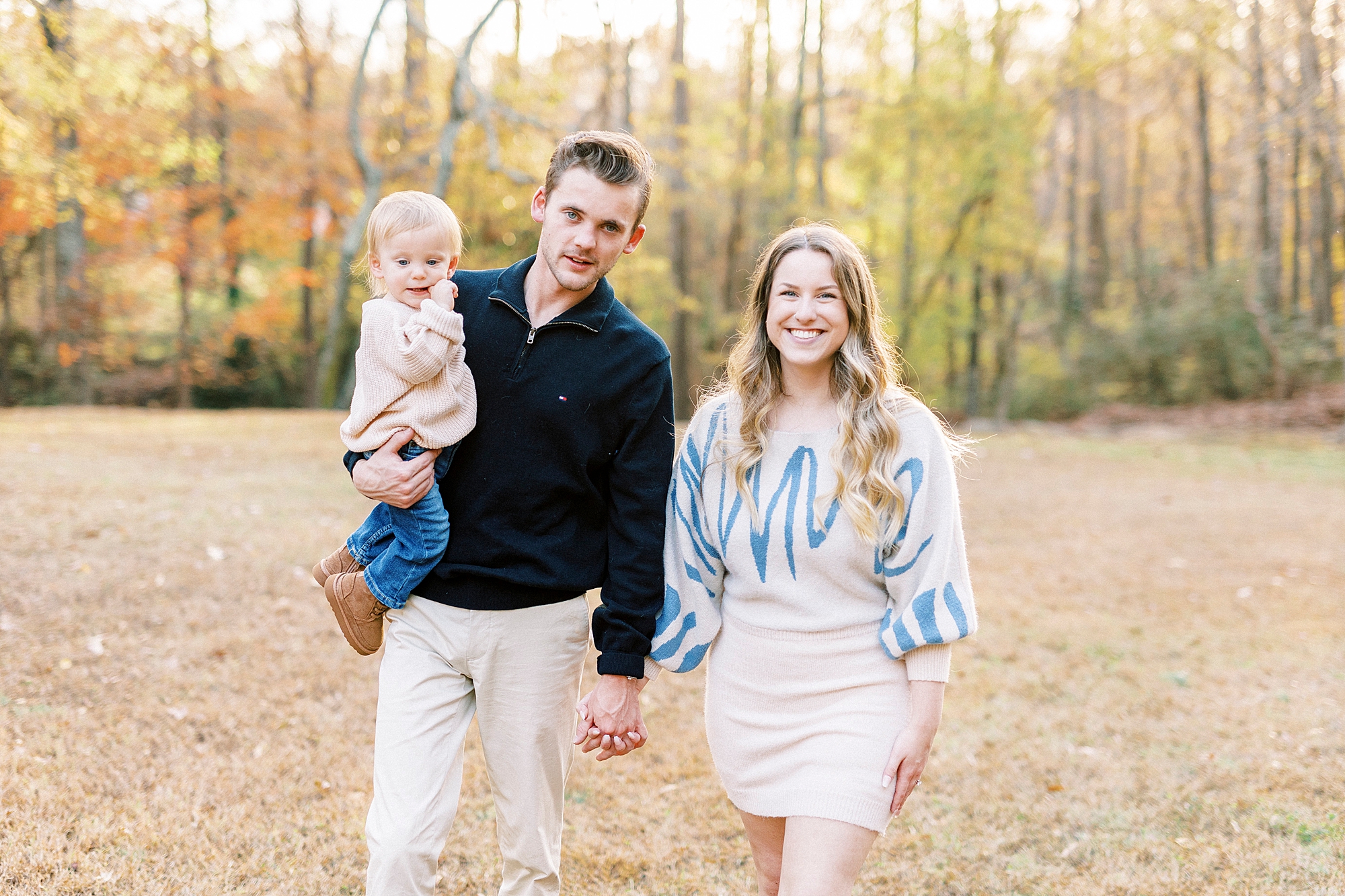 mom and dad hold hands walking with son on dad's hip 