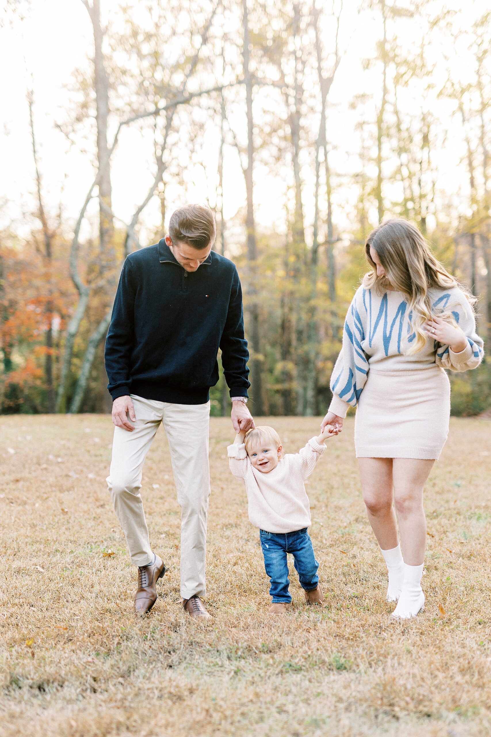couple holds son's hands helping him walk through Baker's Creek Park