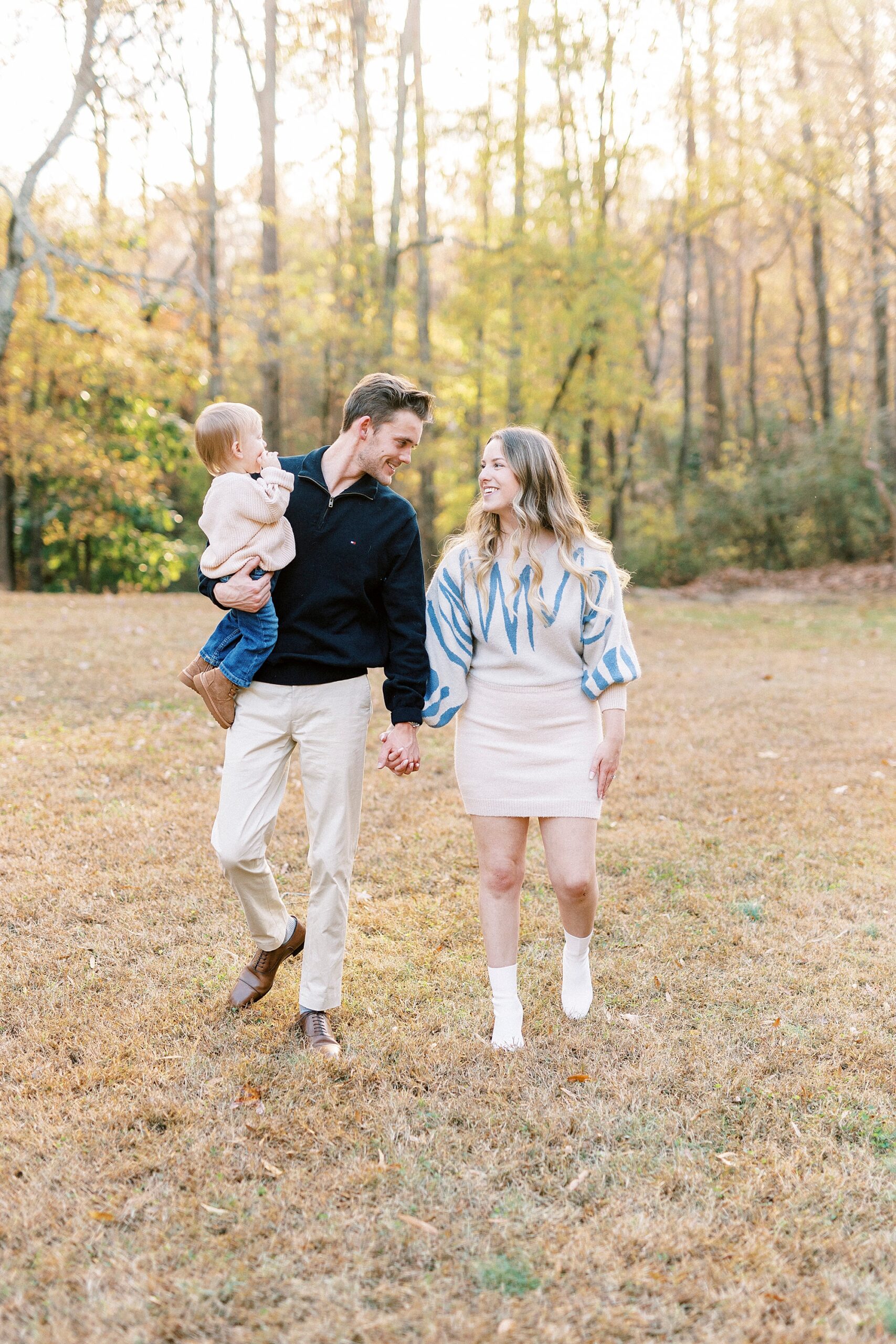 engaged couple holds hands walking through Baker's Creek Park with son on dad's hip