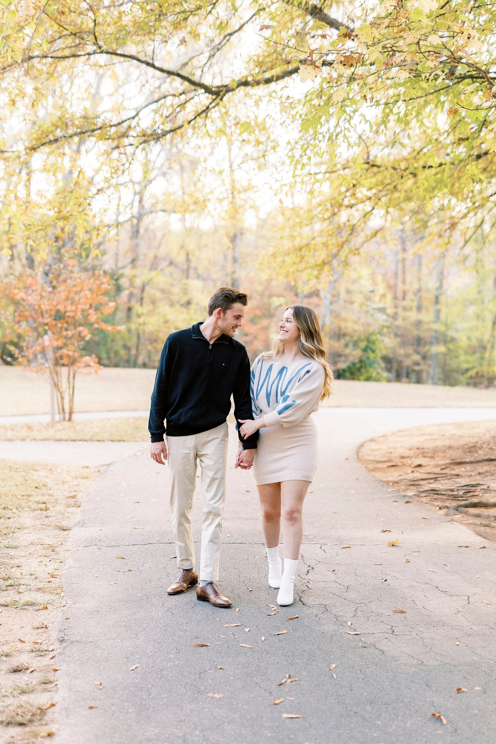 man and woman hold hands on path in Baker's Creek Park laughing together 