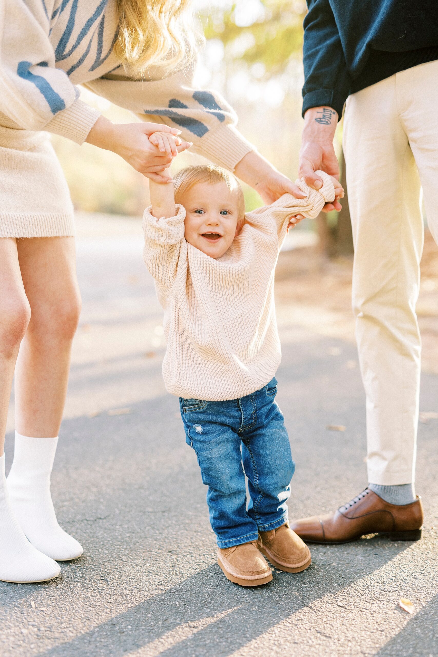 couple holds son's hands to help him stand during fall family photos 