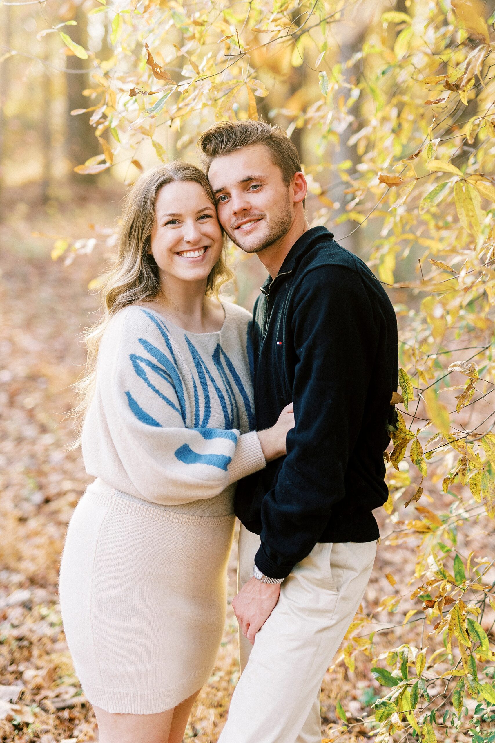 engaged couple leans together in yellow leaves of trees at Baker's Creek Park